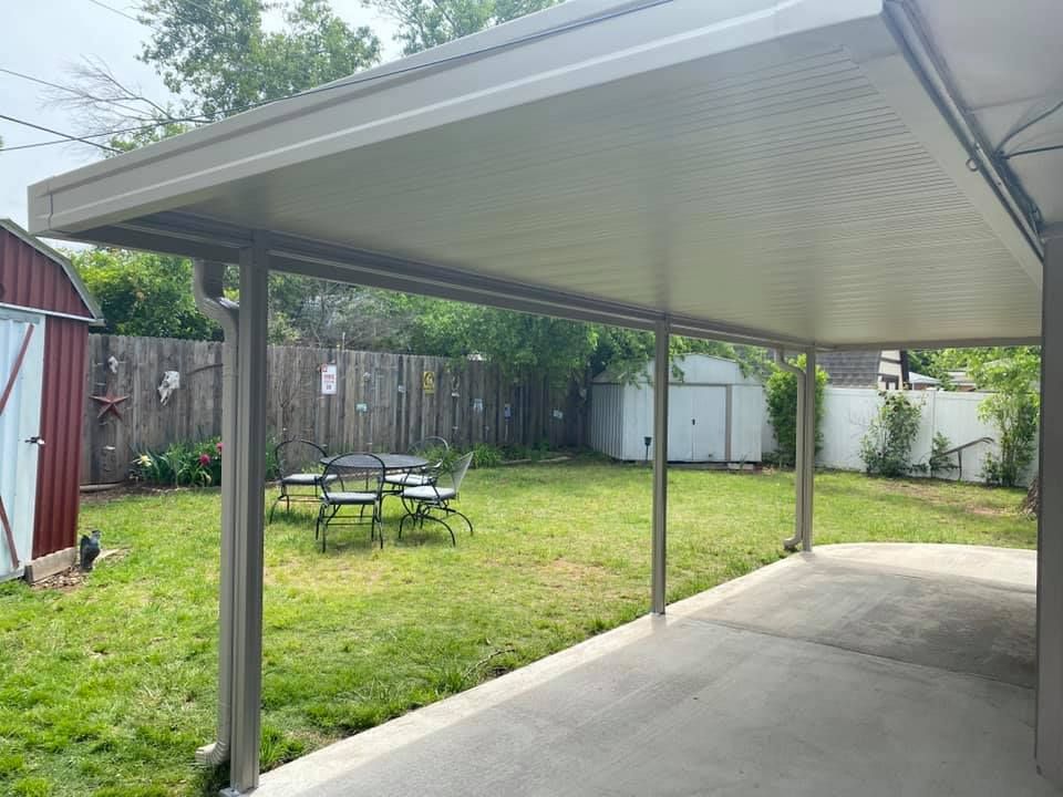 Covered patio beside a grassy backyard with a table and chairs, fenced yard, and small shed in the distance.