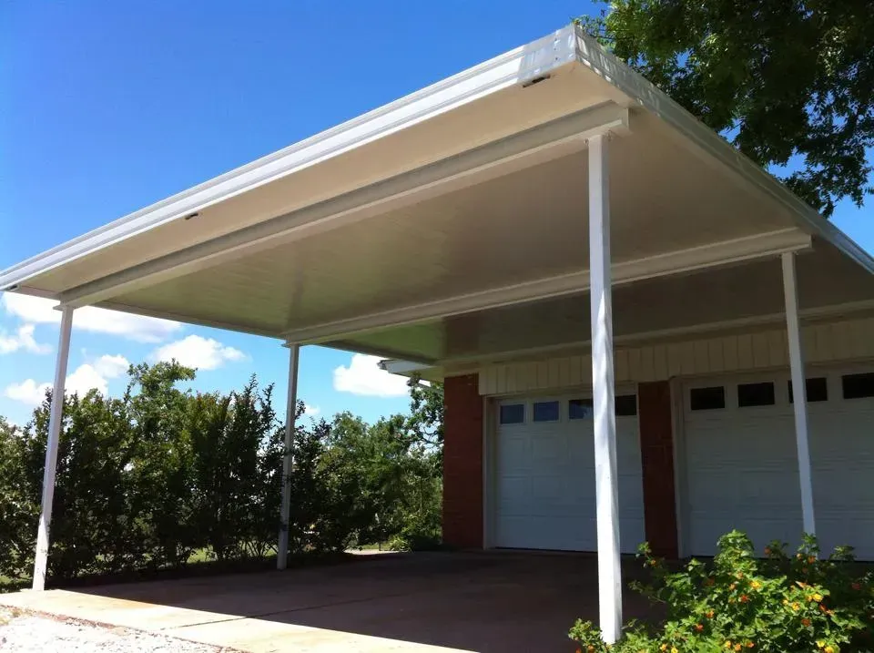 Covered driveway carport beside a house with white posts and beige roof under a blue sky
