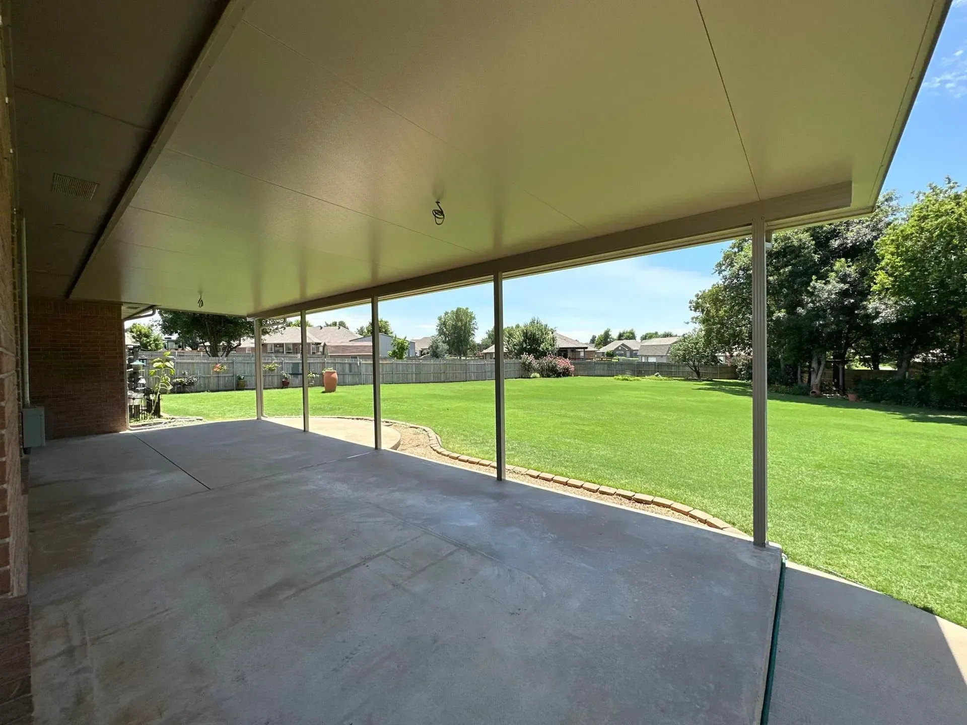 Covered patio overlooking a green lawn and trees under a clear blue sky