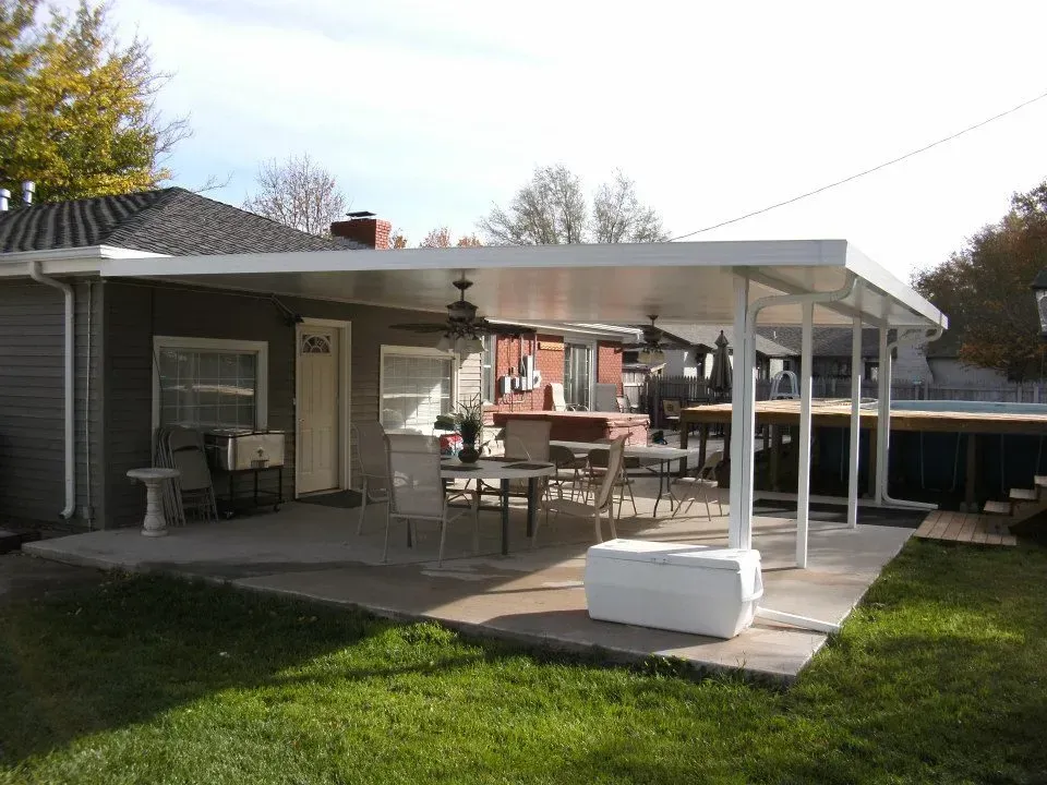 Backyard patio with a covered seating area, grill, and white storage bench beside a grassy lawn.