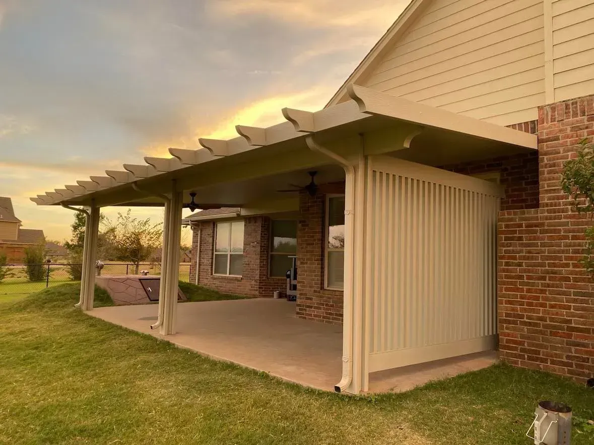 Covered backyard patio with brick pillars, beige awning, and grassy yard at sunset