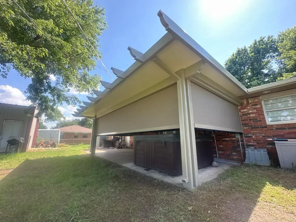 Detached carport with a raised roof and open sides beside a brick house on a grassy yard