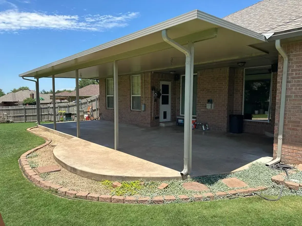 Covered brick patio with metal posts and curved concrete edge beside a house