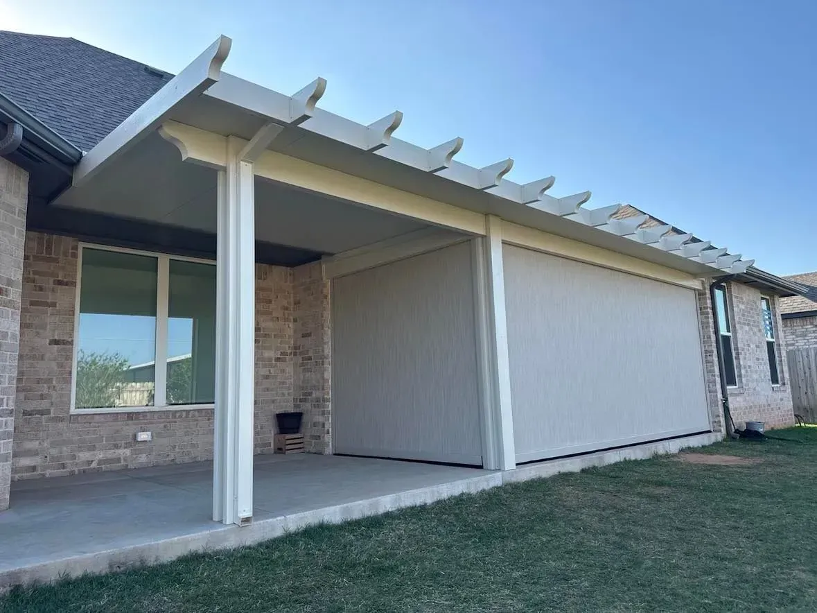 Covered patio with beige columns and privacy screen beside a brick house under a clear blue sky