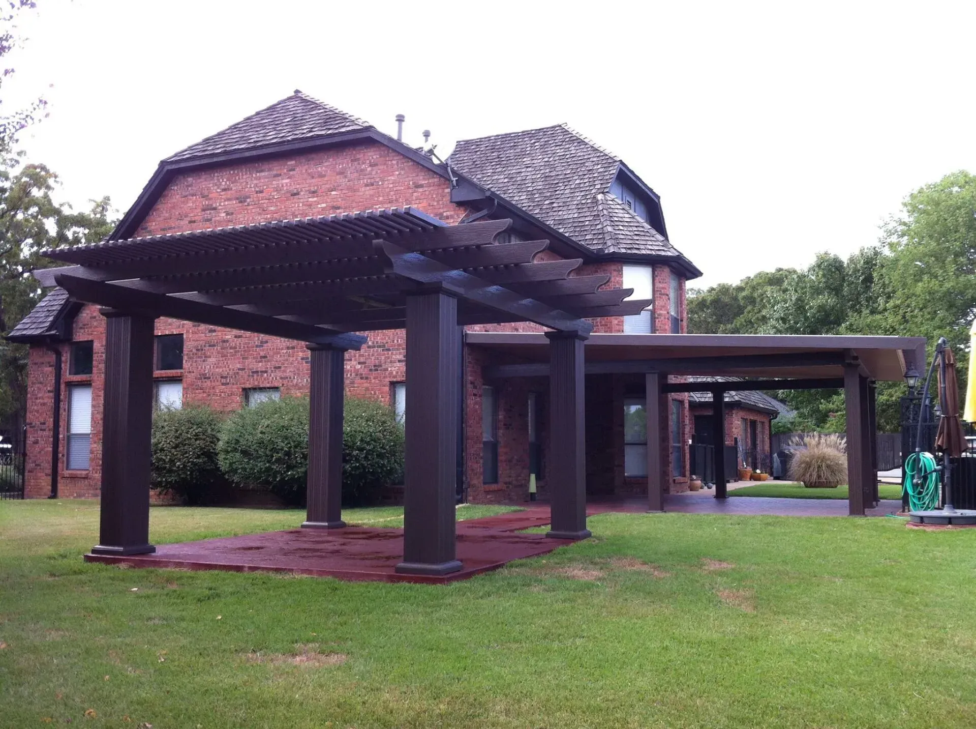 Red brick pavilion with dark wooden columns and roof, set in a grassy park area