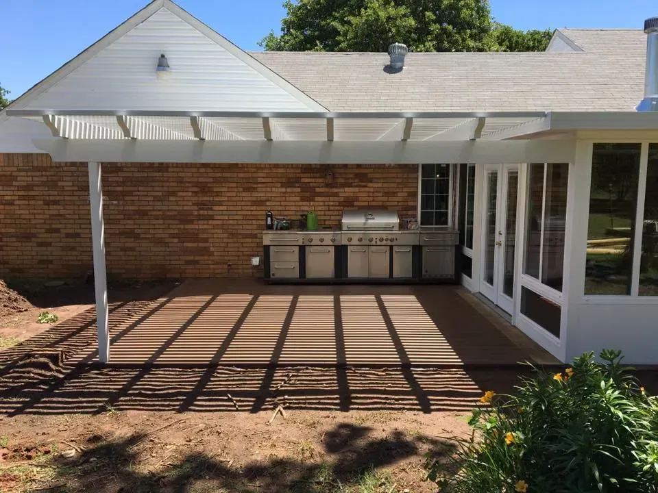 Covered patio with pergola, brick wall, and outdoor cabinets beside sliding glass doors