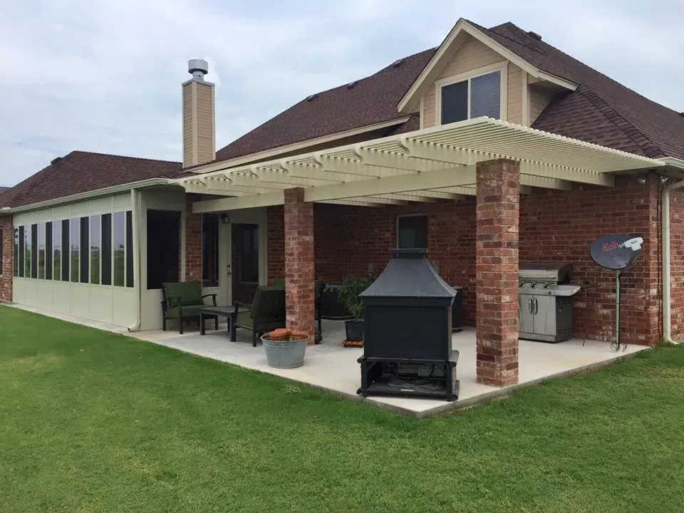 Backyard patio with brick columns, outdoor grill, chimney, and covered seating area beside a house