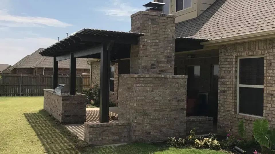 Brick house patio with covered porch, chimney, and a grassy backyard.