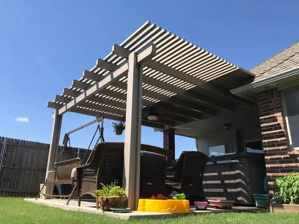 Backyard patio with pergola, wicker chairs, grill, and a yellow kiddie pool on a sunny day