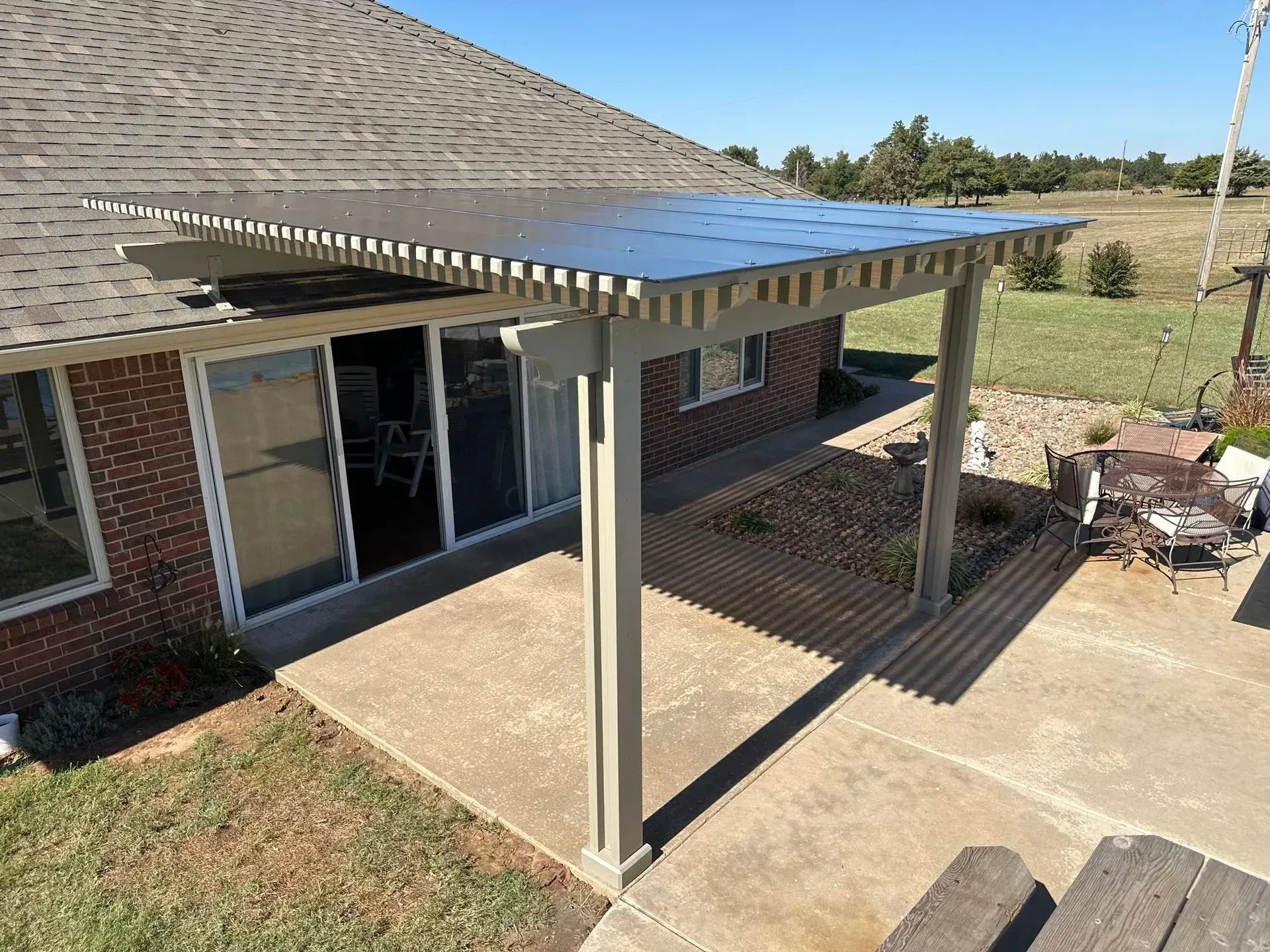 Back patio with a metal pergola covering a concrete slab beside a brick house and sliding glass door