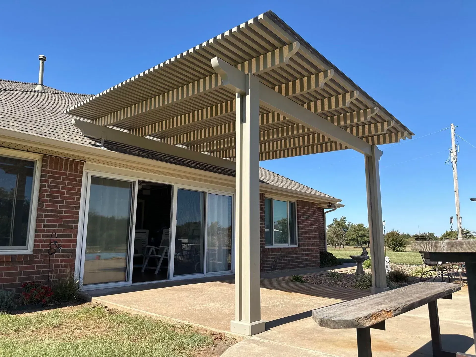 Backyard patio with a wooden pergola attached to a brick house, beside sliding glass doors.