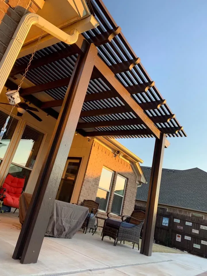 Patio with wood pergola, outdoor seating, and stone fire pit beside a house at sunset