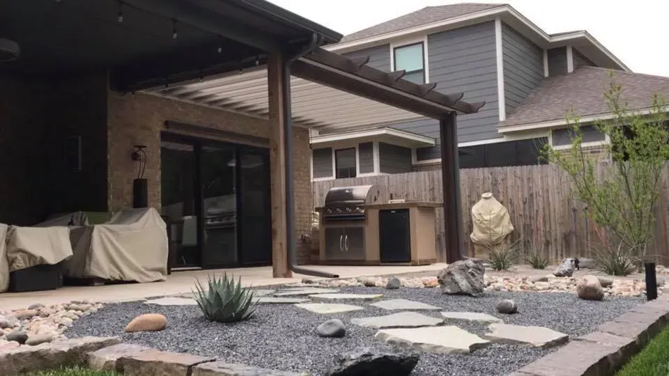 Backyard patio with covered seating, outdoor grill, and xeriscape rock garden beside a house