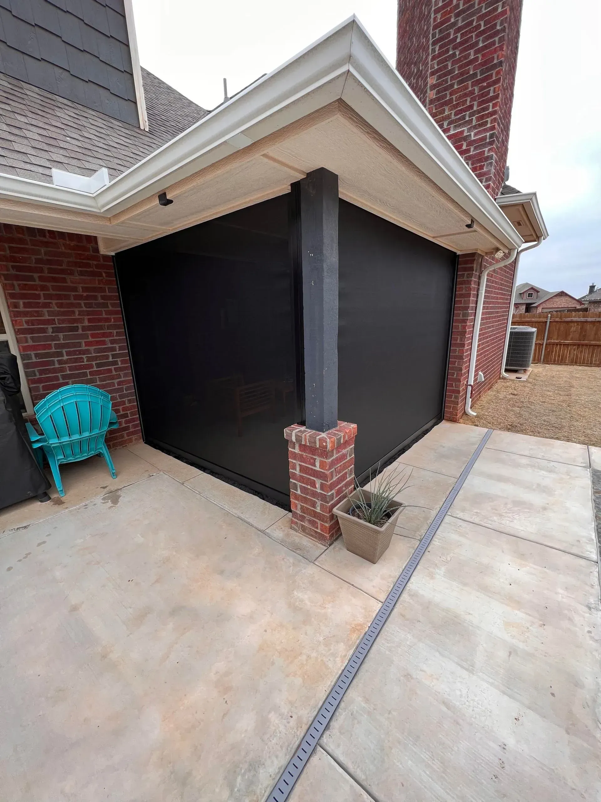 Brick house porch with black screened enclosure, turquoise chair, and concrete walkway