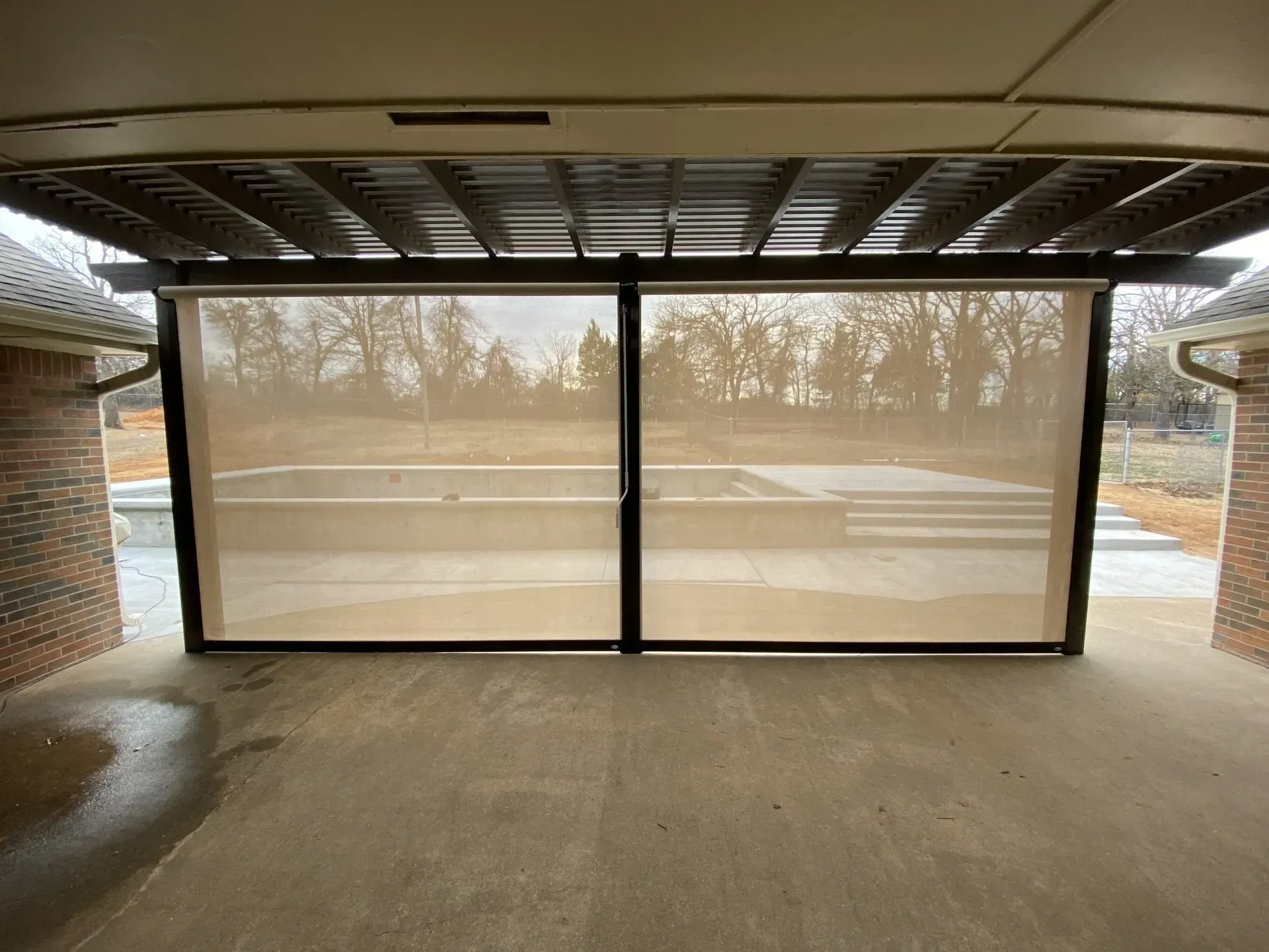 Empty covered patio facing a road, with black-framed glass panels and a wet concrete floor