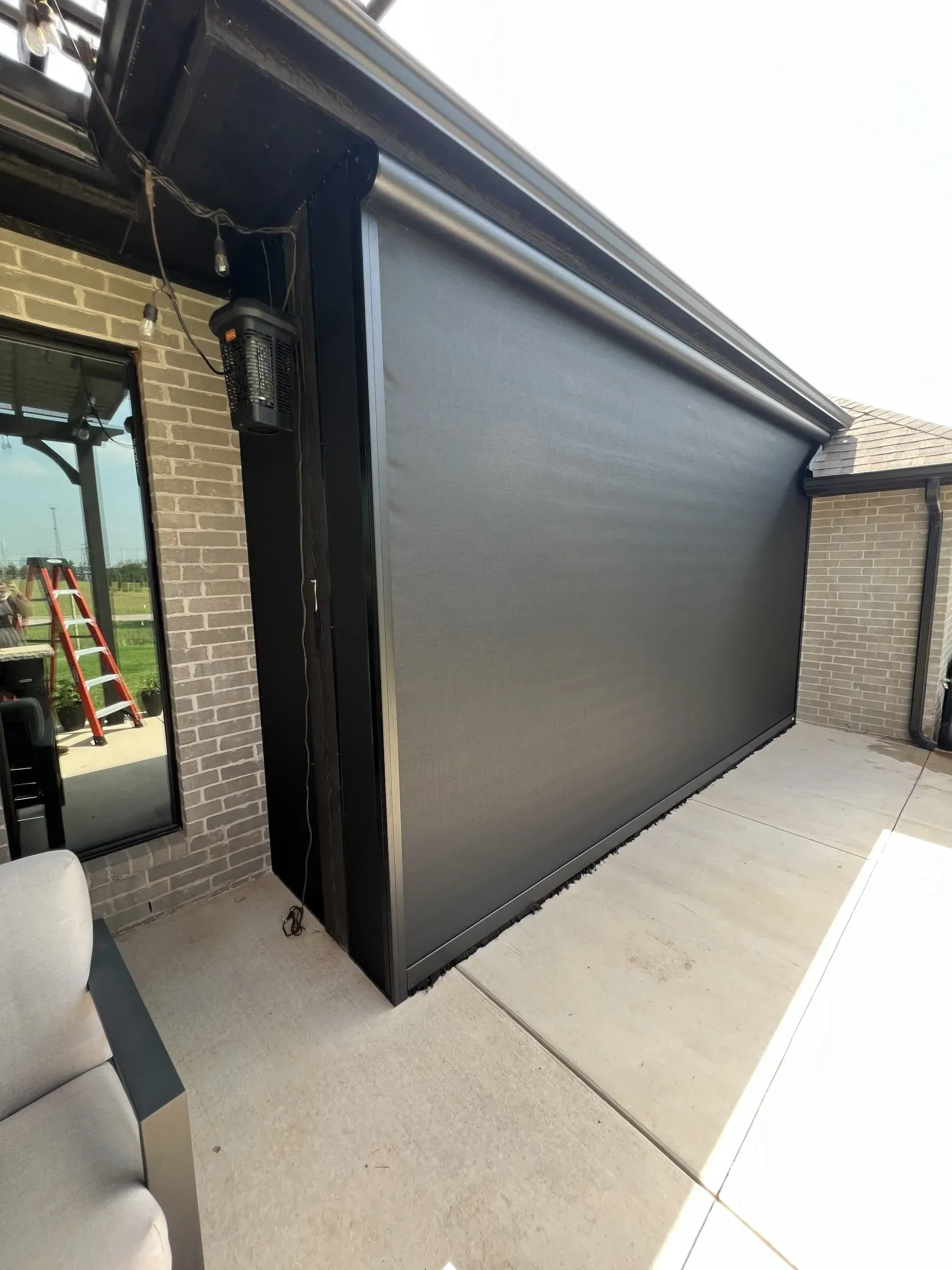 Black patio retractable screen shade beside a house, covering an outdoor opening