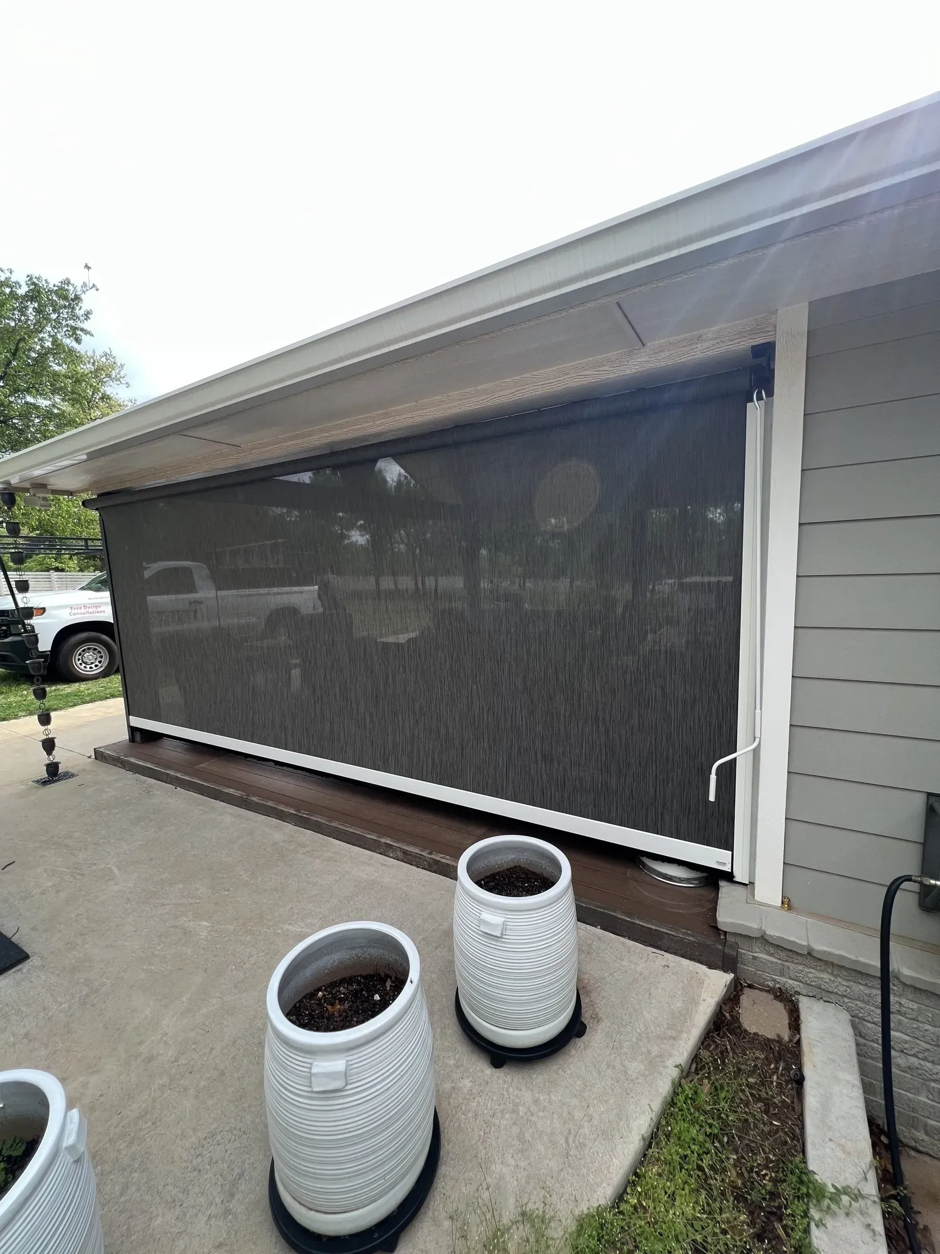 Patio with black mesh shade curtain along a house, two white planters, and a concrete walkway