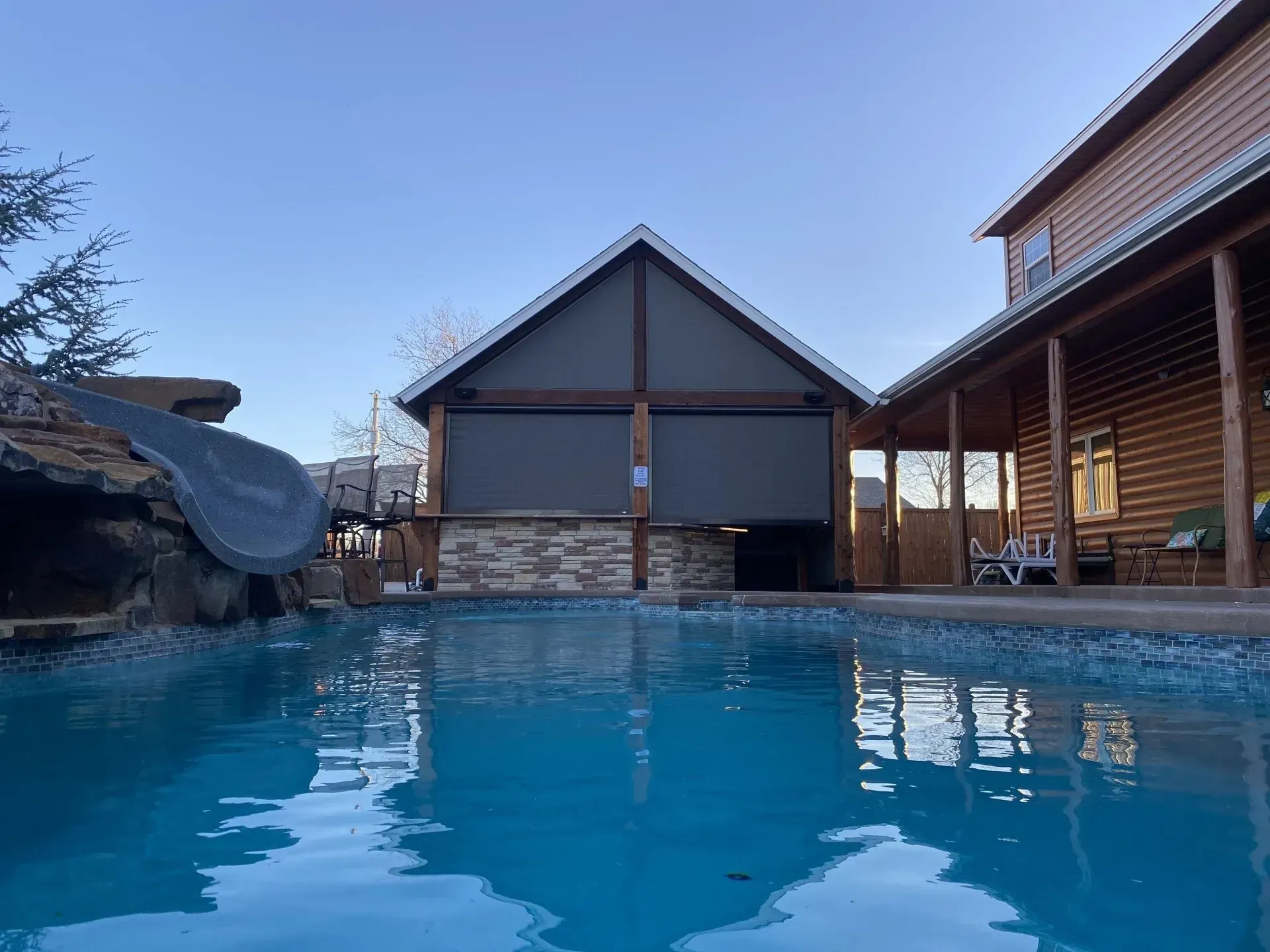 Blue swimming pool with lounge chairs and a covered patio beside a house