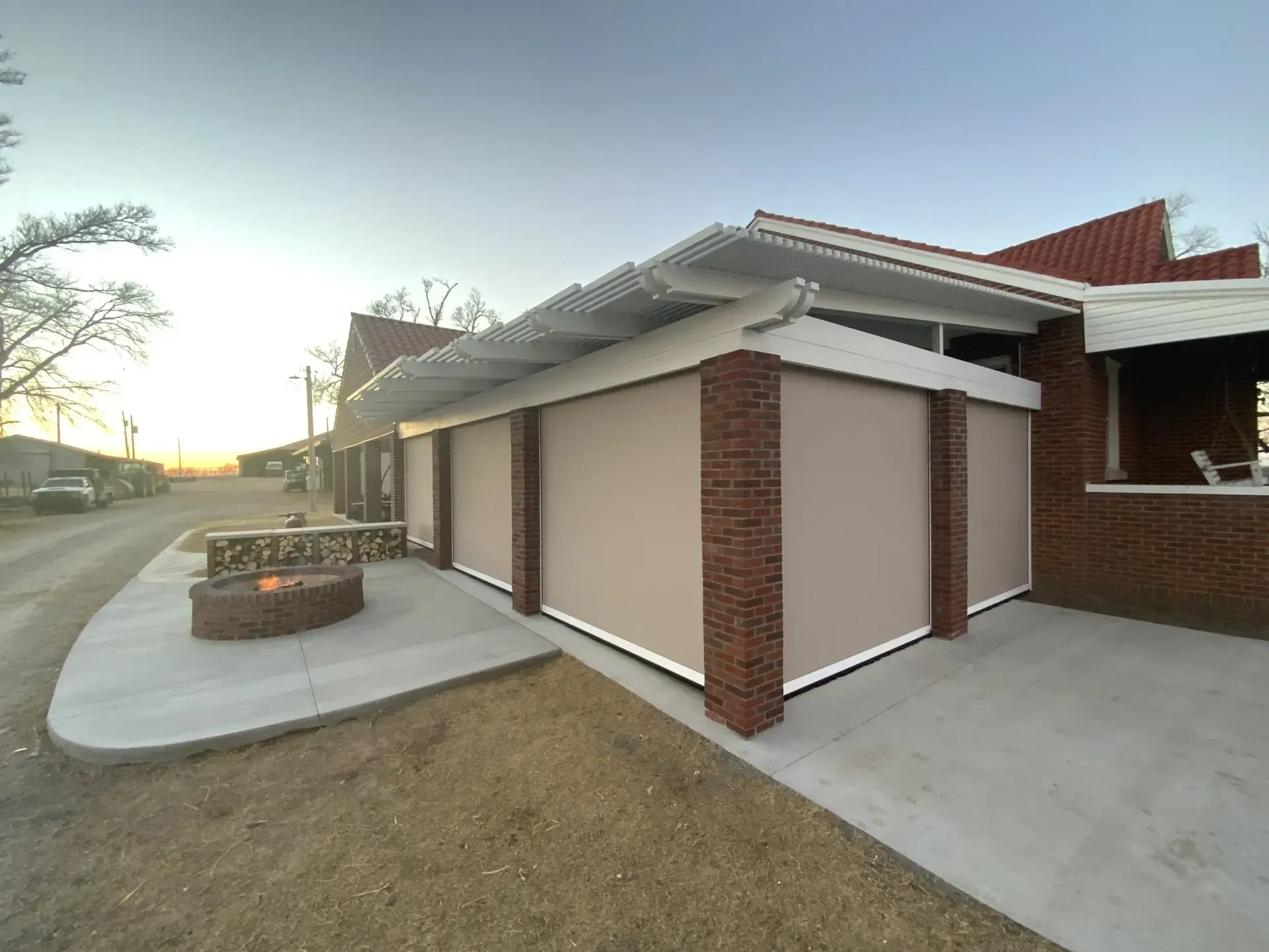Suburban house exterior with beige walls, brick columns, and a curved concrete walkway at sunset
