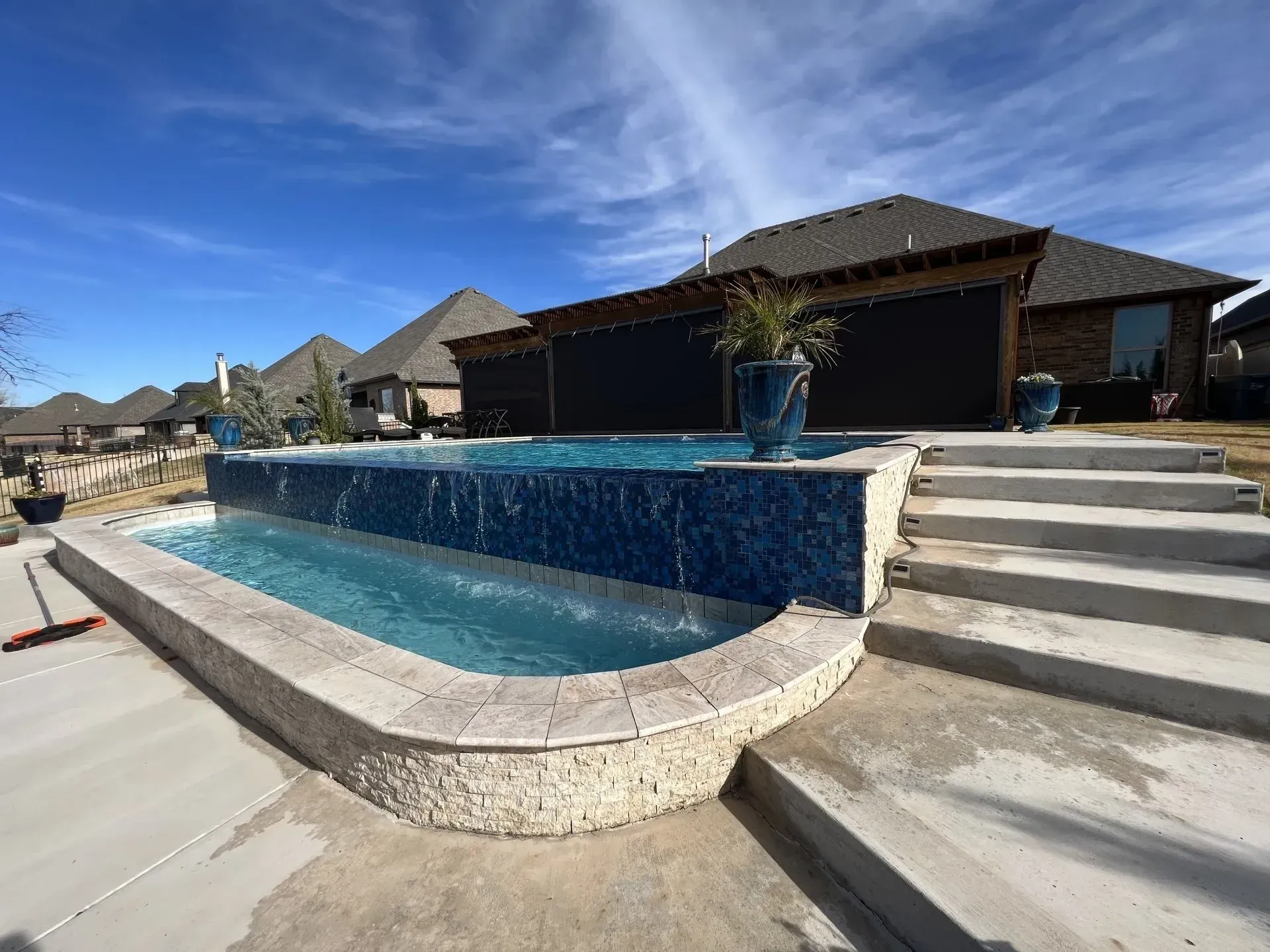 Backyard pool with stone waterfall, steps, and a clear blue sky behind a house
