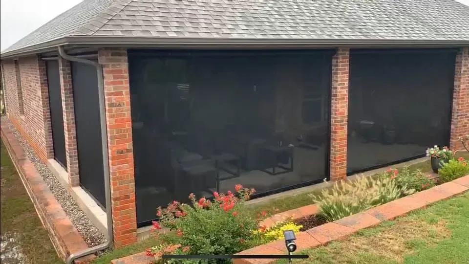 Screened porch with brick columns, dark mesh panels, and flower beds along the front of a home