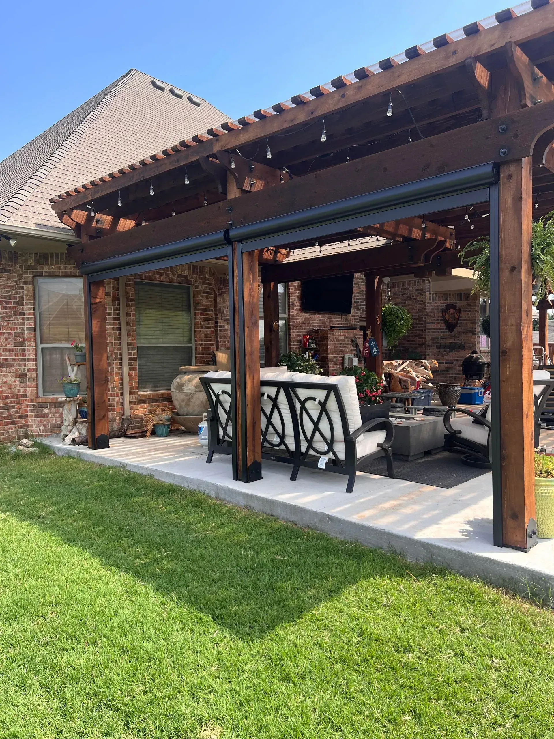 Covered patio with brick seating, wooden beams, and a green lawn beside a house