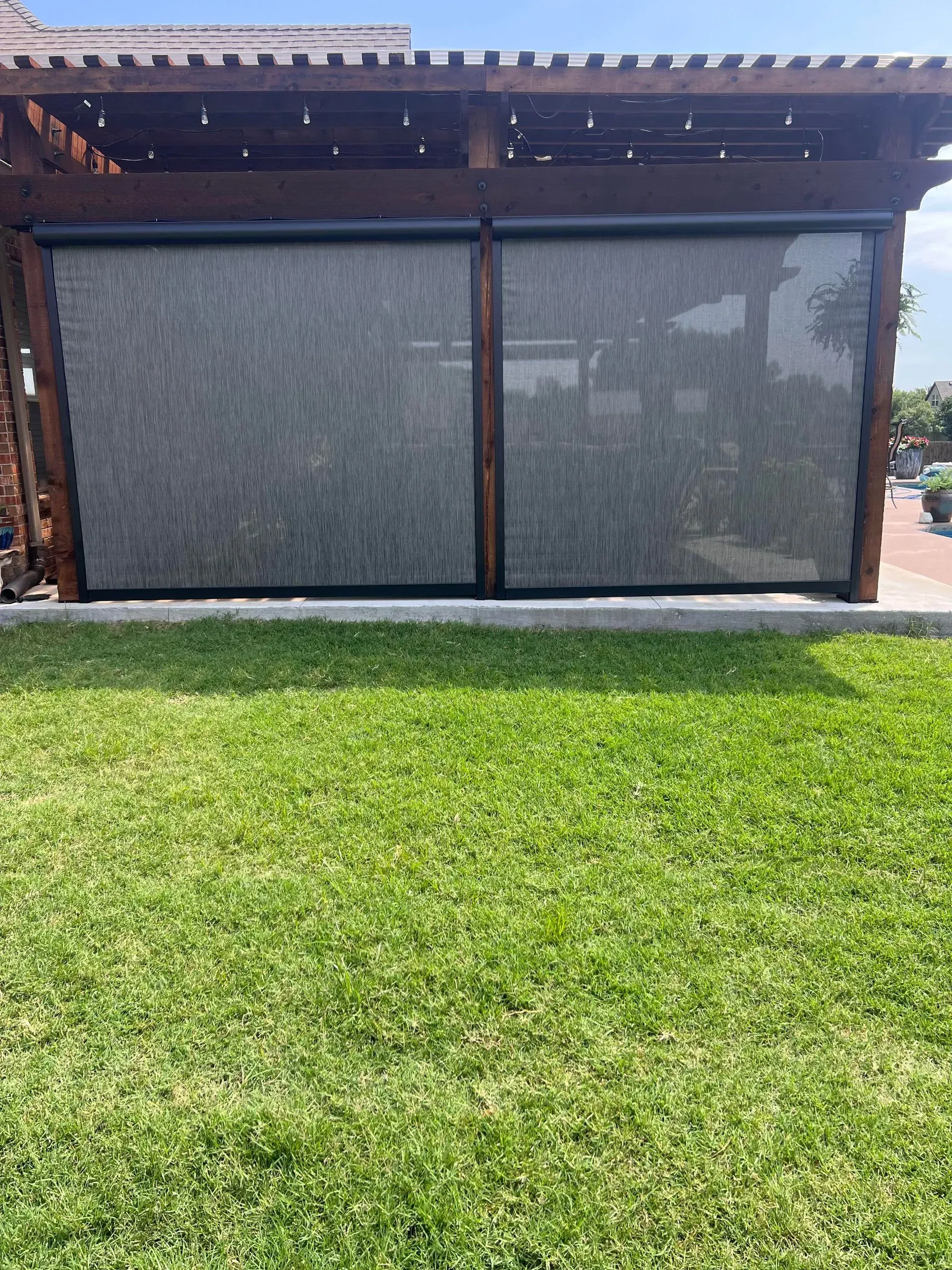 Two-panel outdoor shade screen under a wooden patio roof above a green lawn.