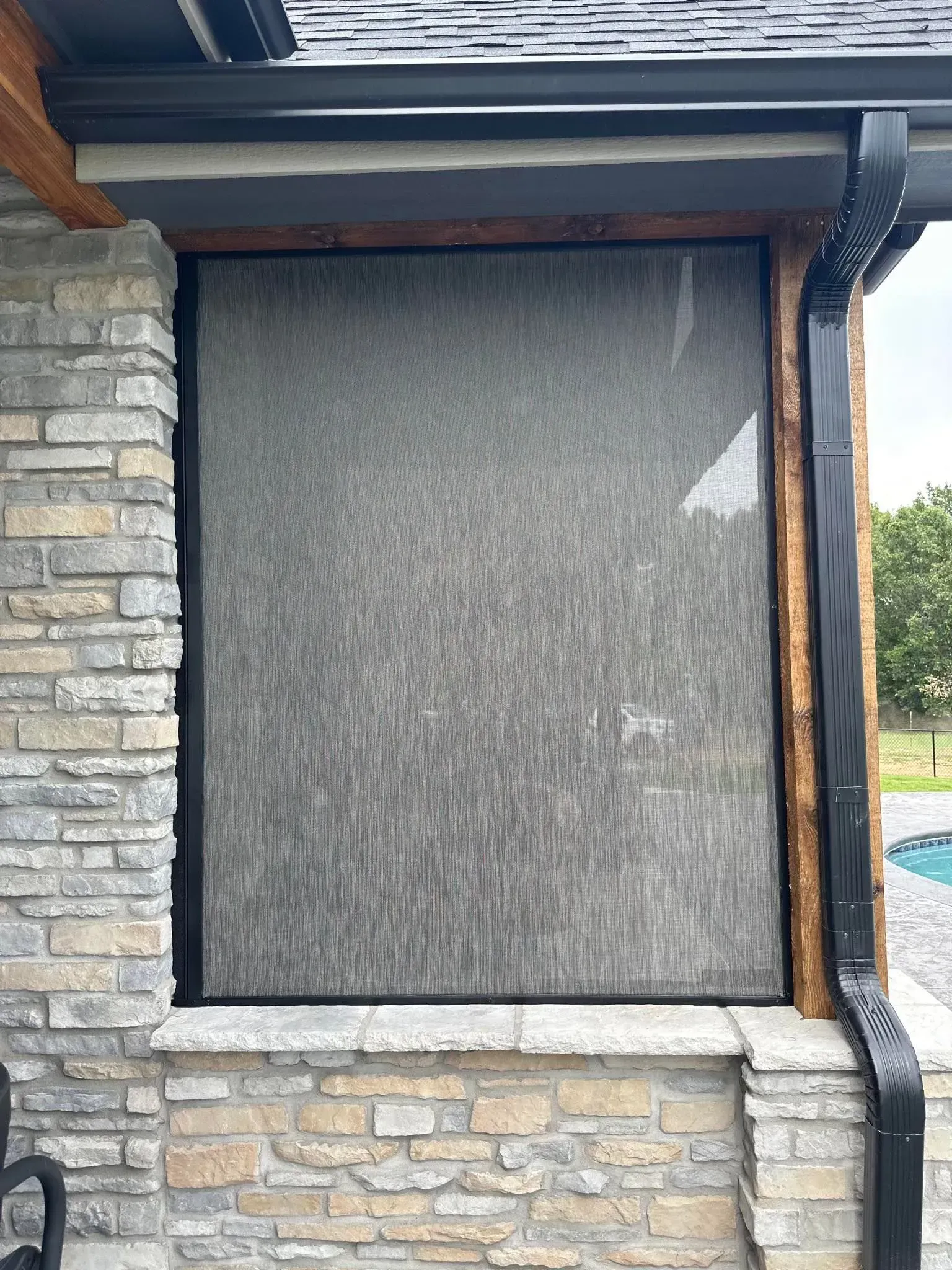 Stone house exterior with a large screened window and black trim under a covered roof.