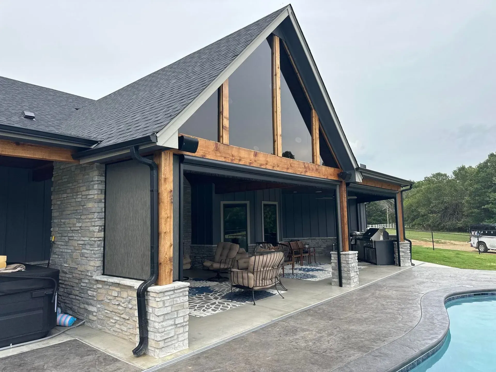 Two-story house with gabled roof, stone accents, covered patio, and a swimming pool in the foreground