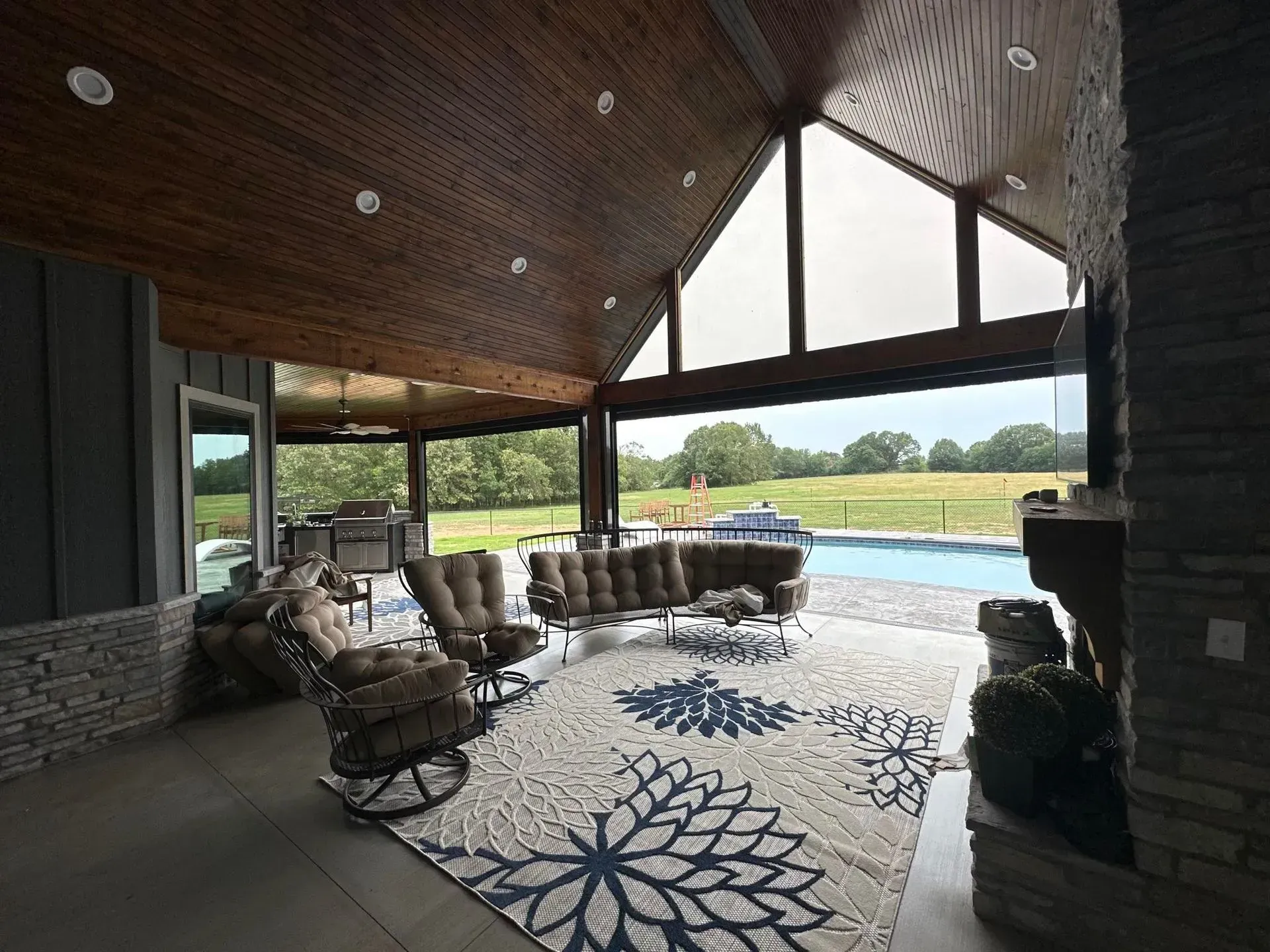 Covered patio with wicker chairs, patterned rug, and an open view of a pool and green landscape.