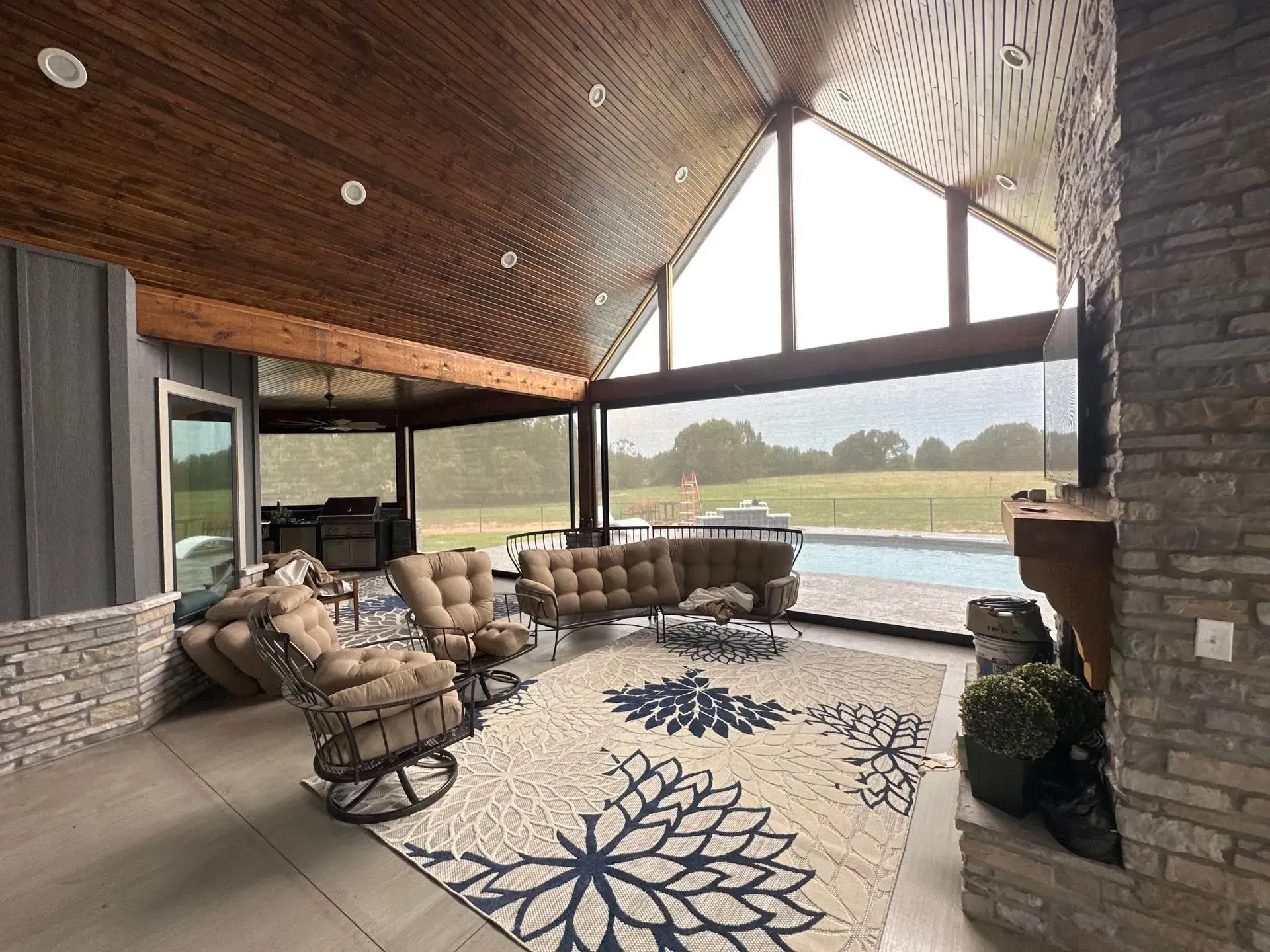 Cozy covered patio with wicker seating, stone fireplace, and lake view through large windows