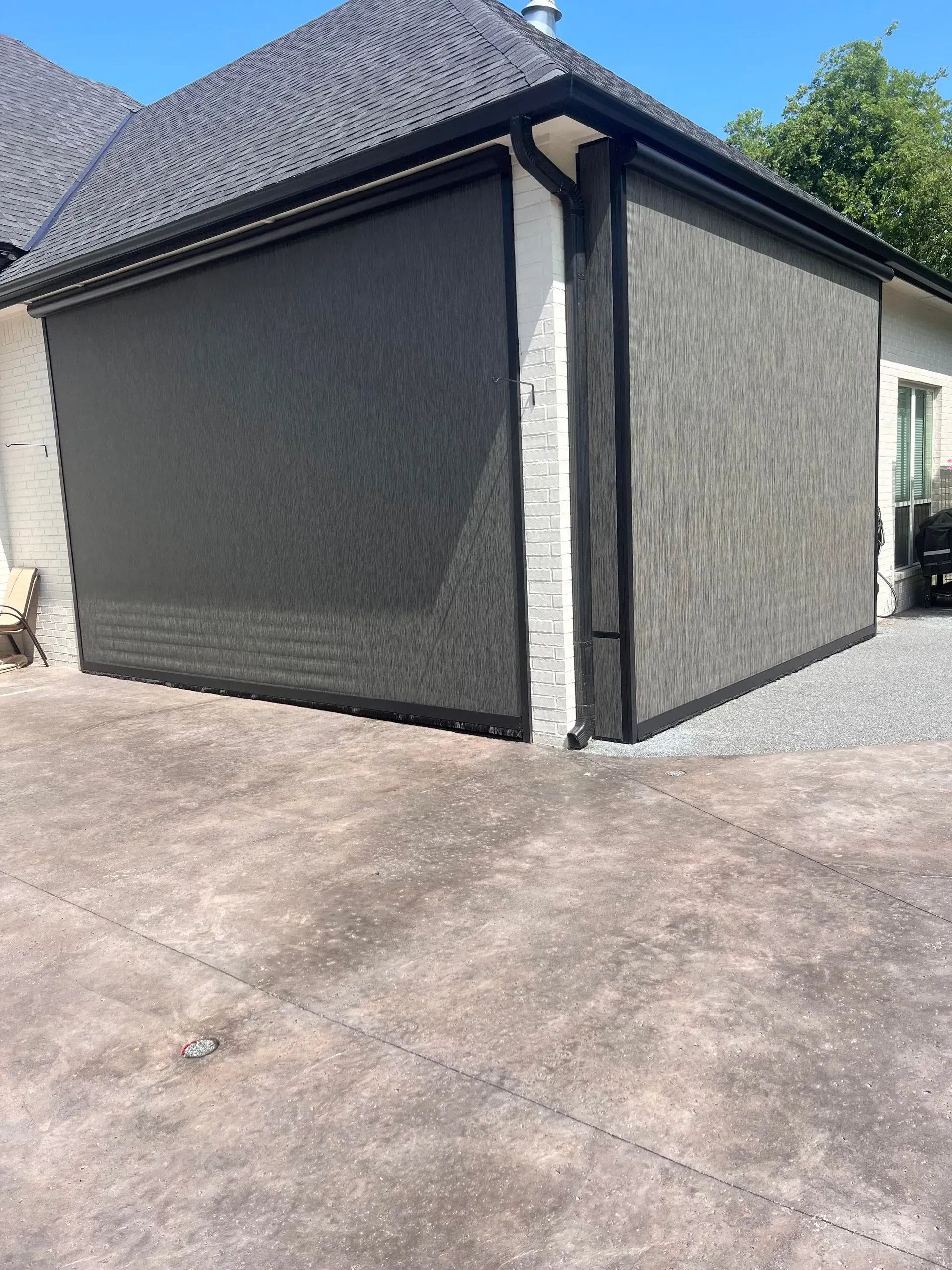 Gray house exterior with dark roof, white trim, and a paved driveway under a sunny sky