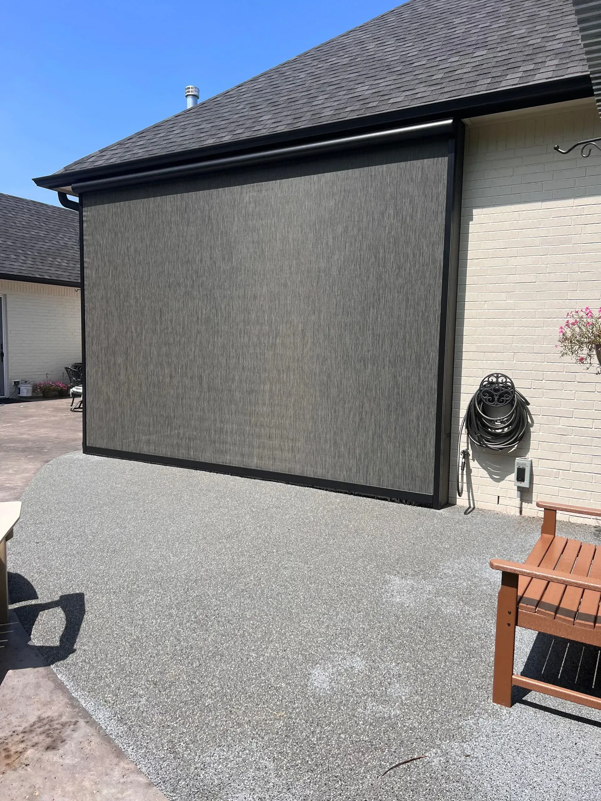 Gravel yard beside a gray house wall and roof, with a coiled hose on the right and outdoor chair in foreground