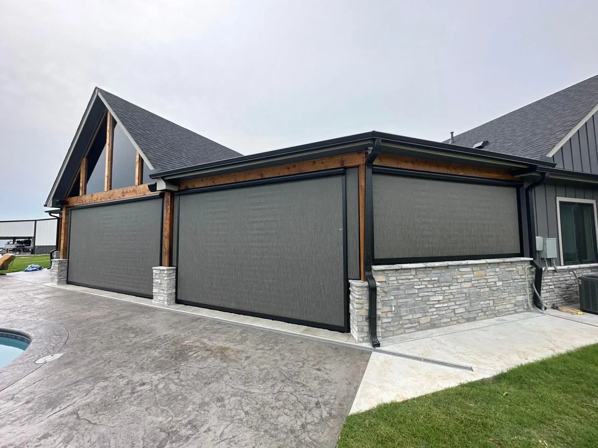 Modern house exterior with dark gray garage-style panels and stone base on a driveway