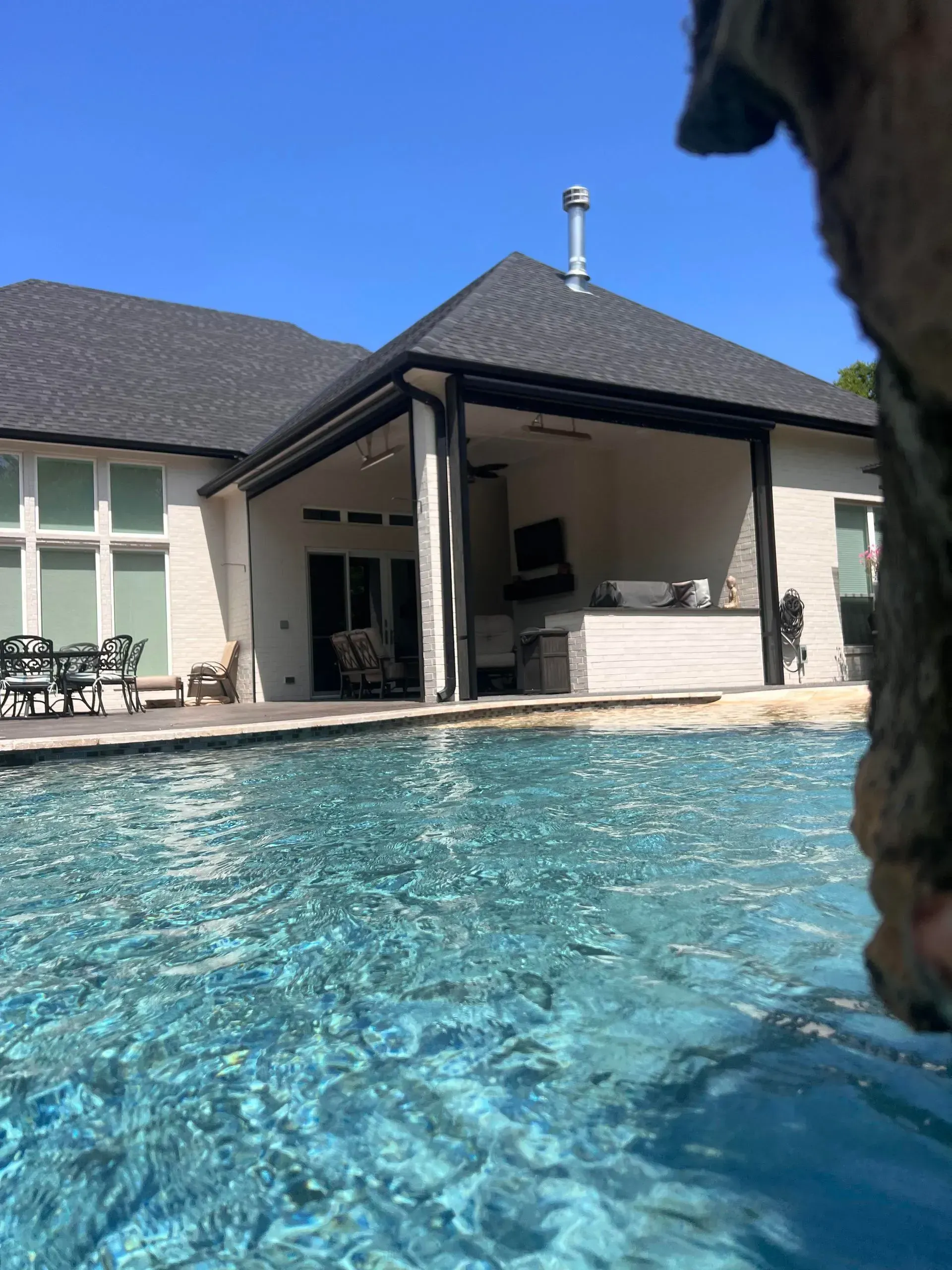 Backyard pool beside a covered patio and house under a clear blue sky
