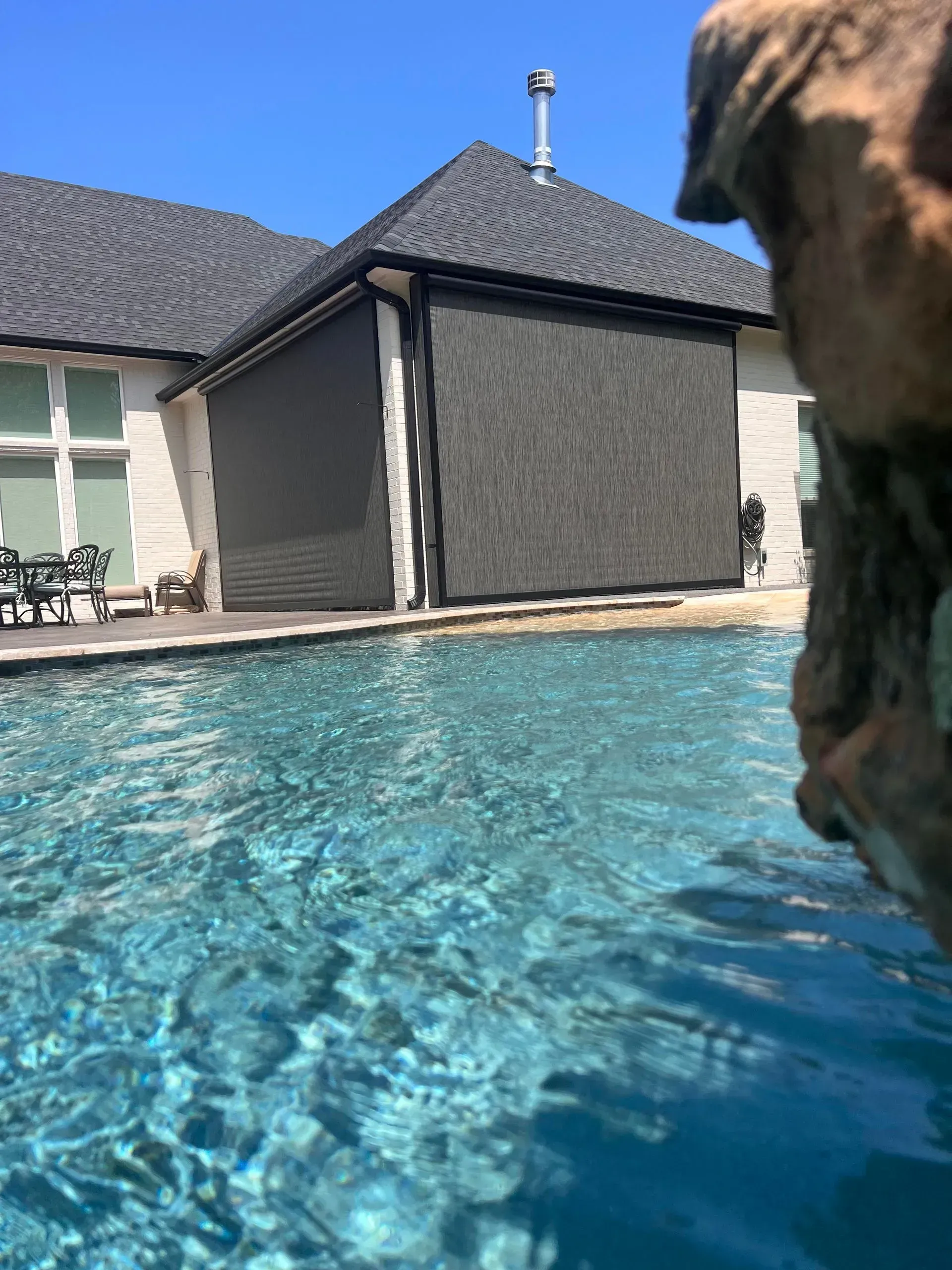 Backyard pool beside a gray house with blue water and clear sky