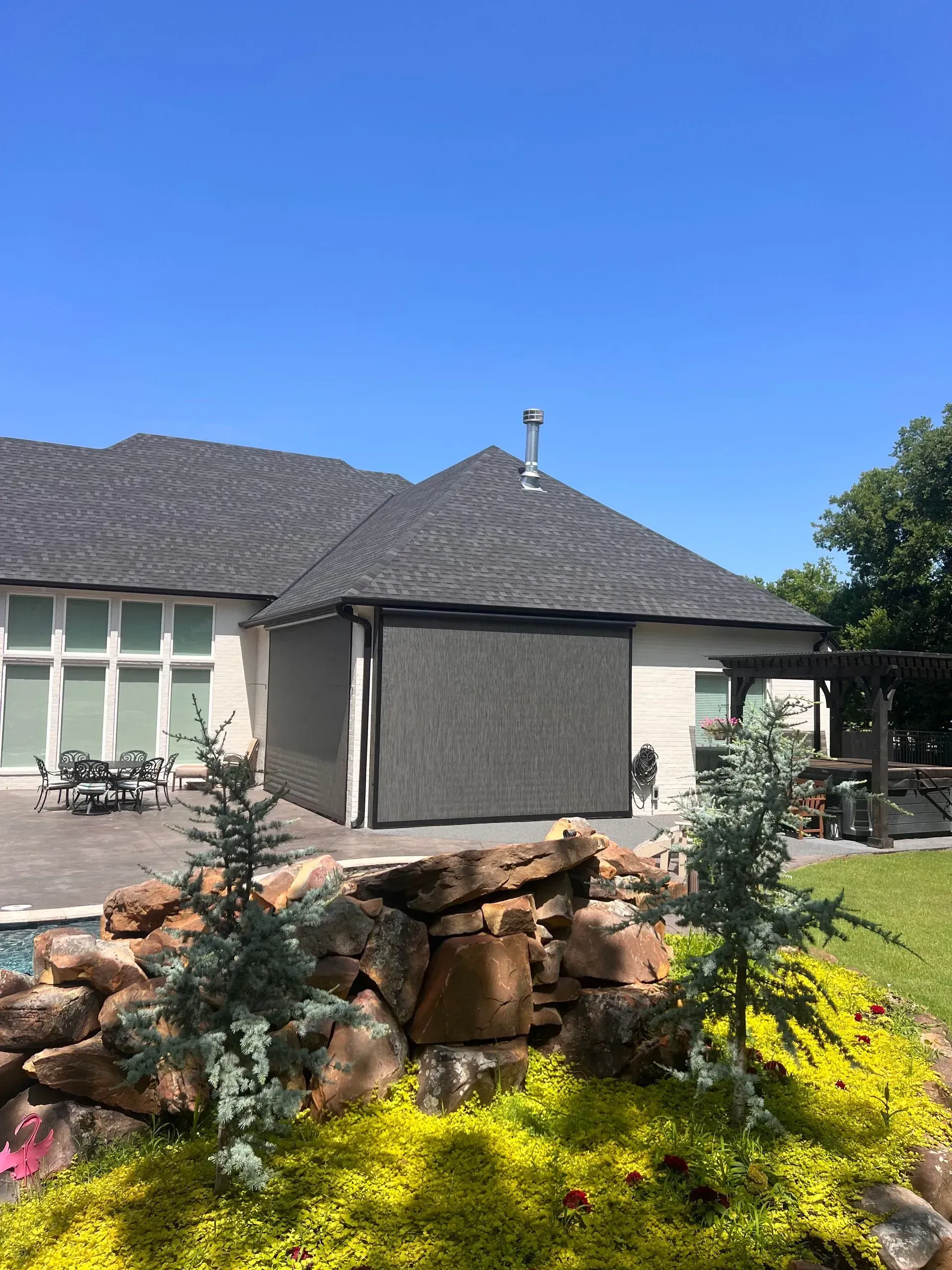 Modern house with dark tiled roof, stone garden wall, and bright yellow flowers under a clear blue sky