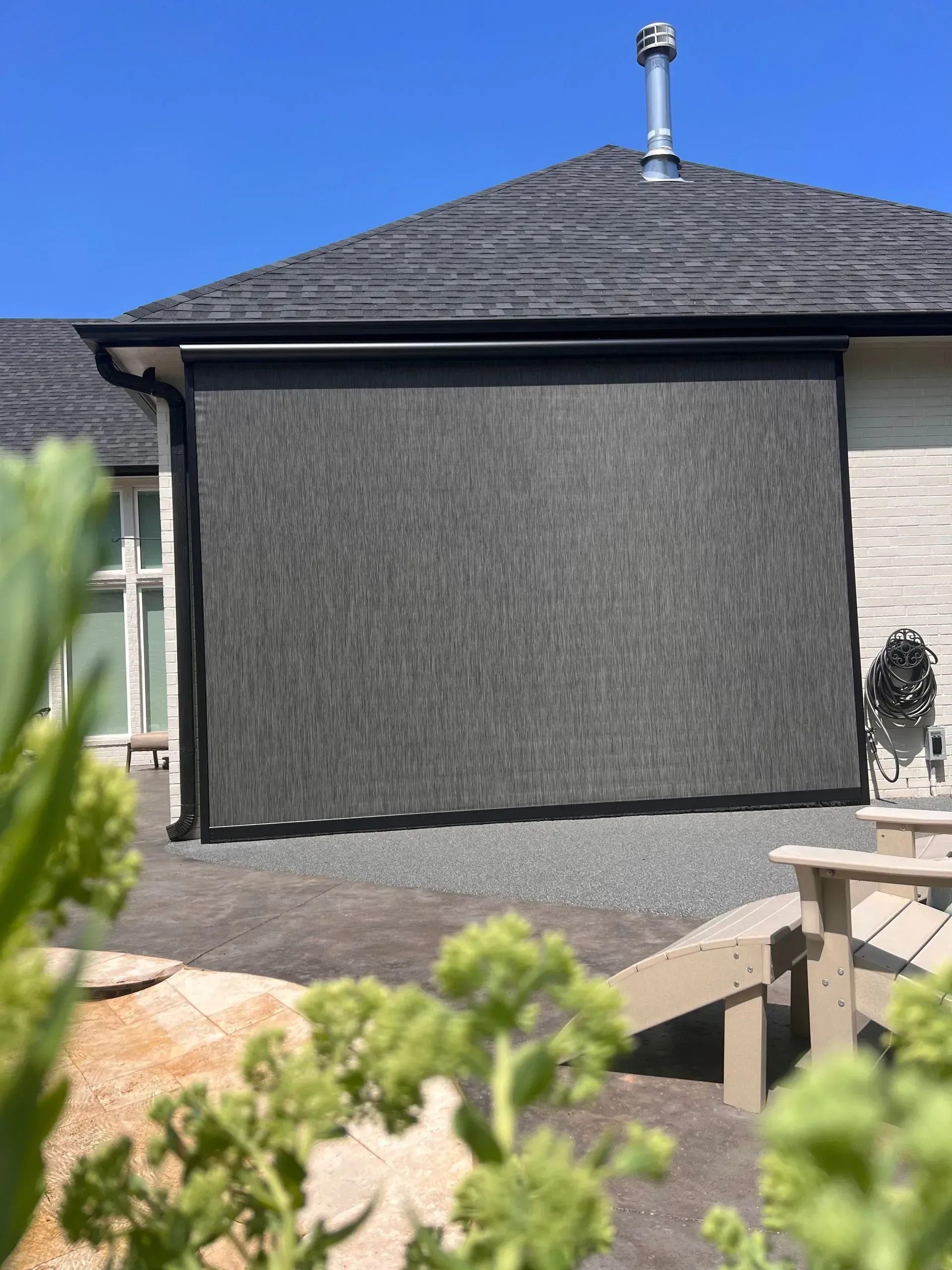 Black privacy screen on a house wall under a dark roof in a sunny backyard