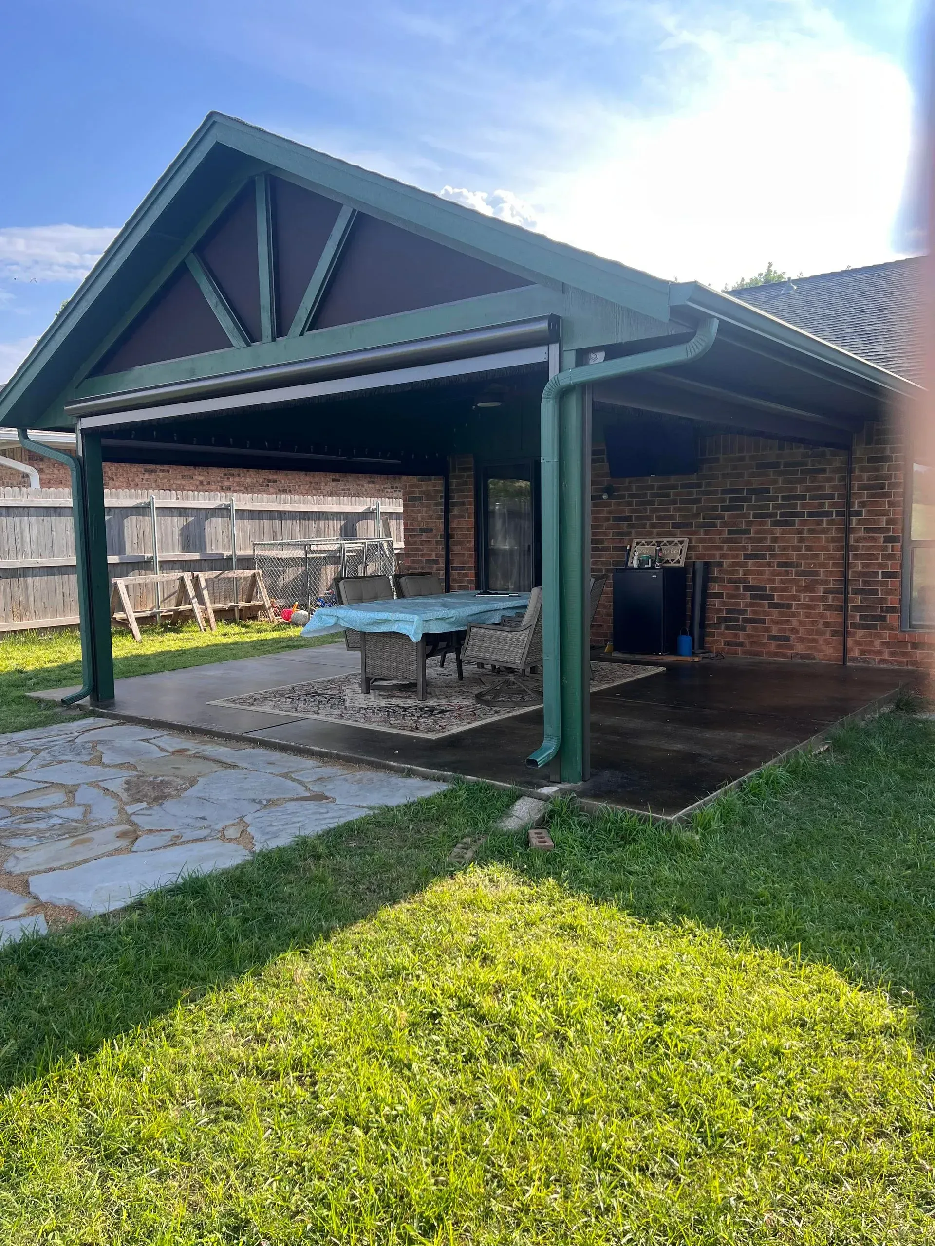 Backyard brick patio with covered pergola, picnic table, and green lawn in sunlight