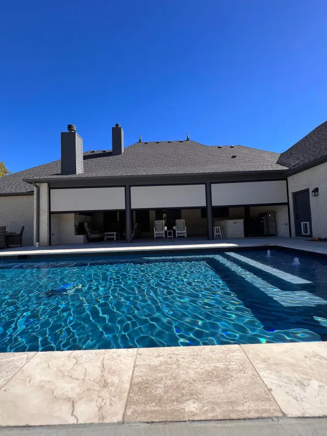Backyard swimming pool beside a covered patio and house under a bright blue sky