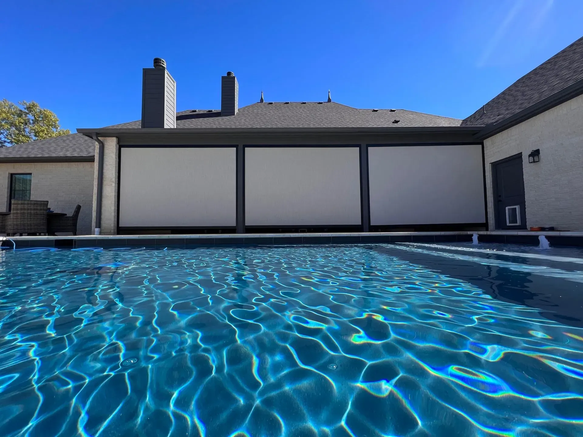Blue swimming pool with rippling water in front of a house under a clear sky