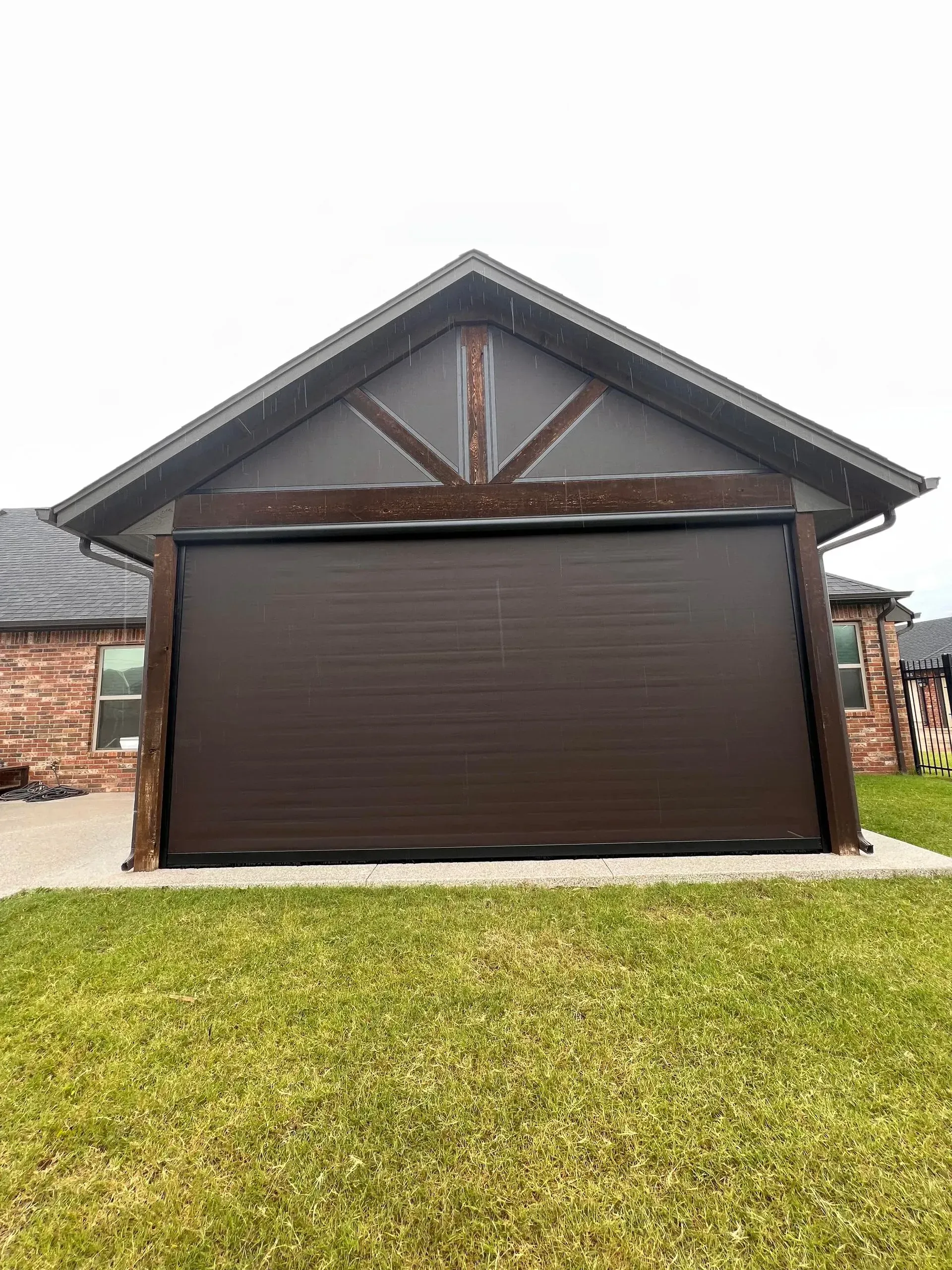 Closed brown garage door on a house with a gabled roof and green lawn in front
