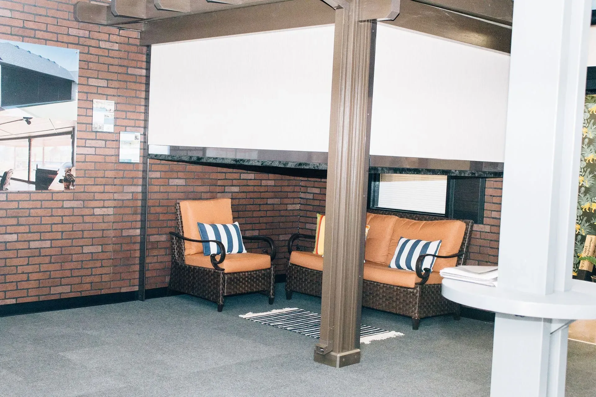 Covered patio seating with two tan chairs, striped pillows, and a wooden post against a brick wall.