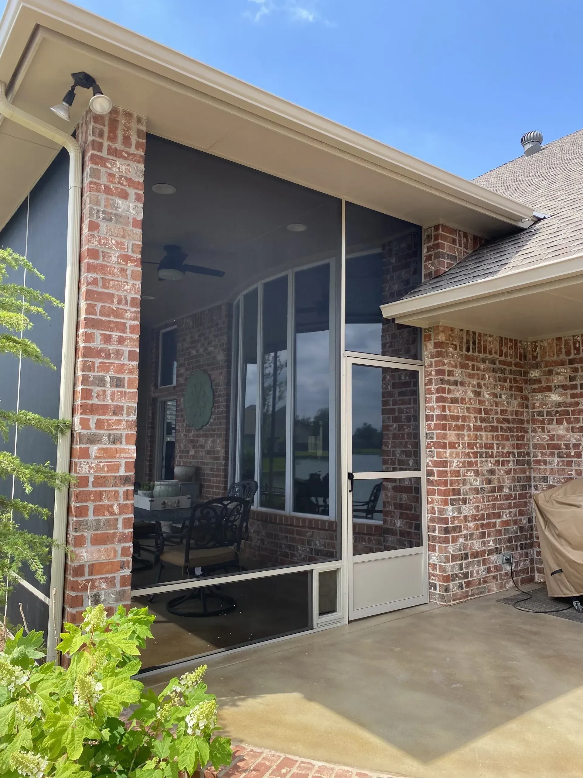 Brick house patio with large screened glass enclosure and concrete floor