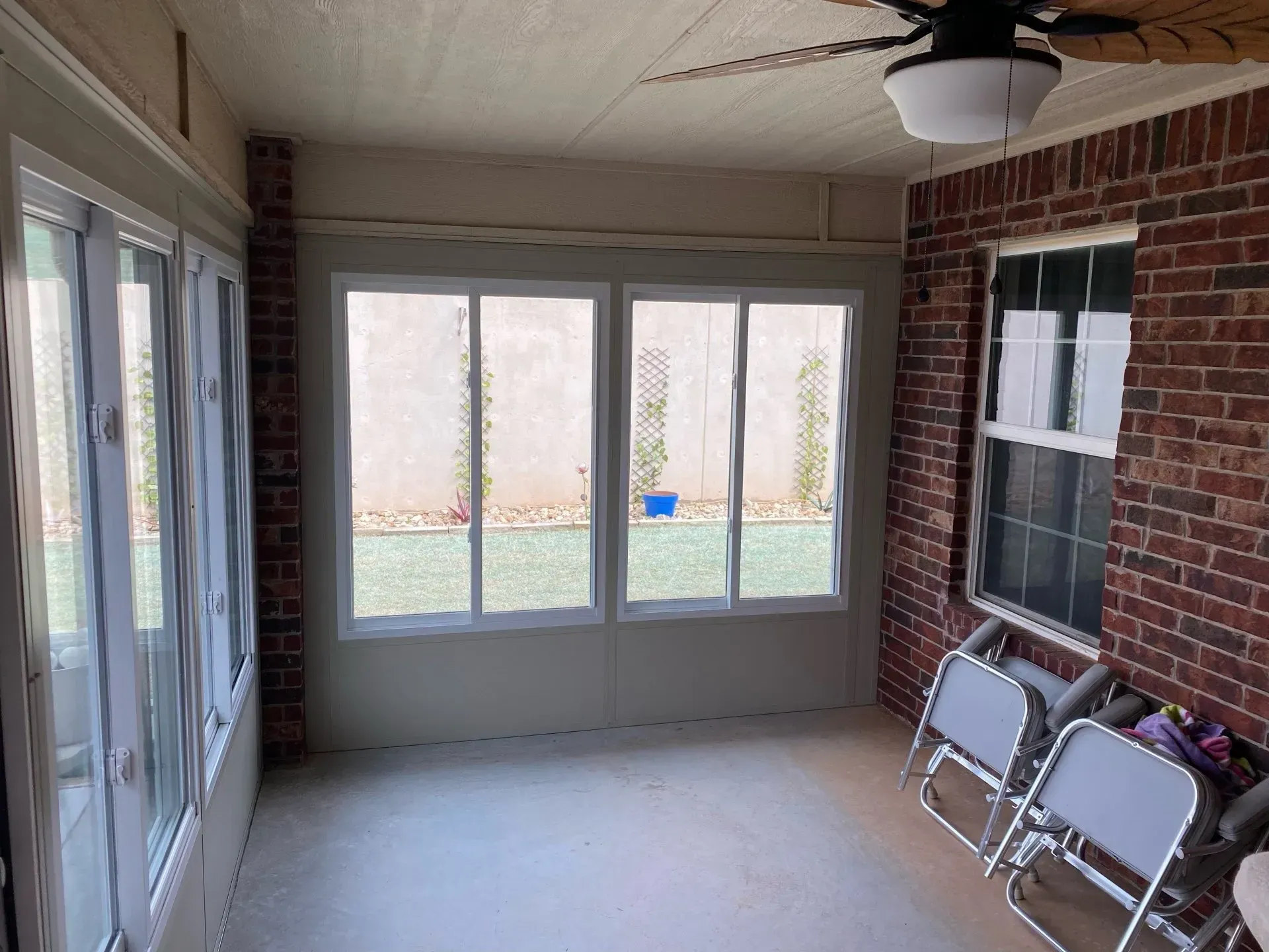 Covered porch with brick walls, white double doors, sliding windows, and two folding chairs on the right.