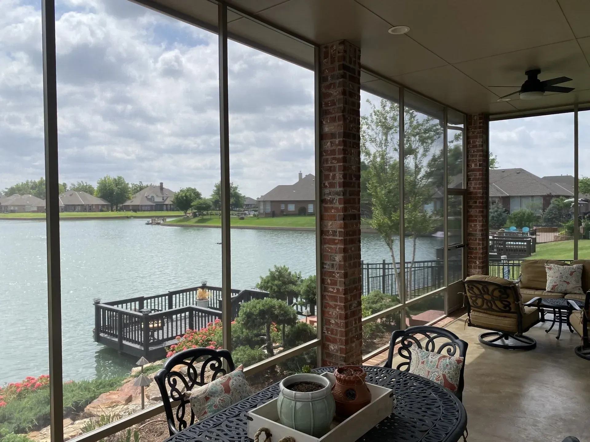 Covered patio overlooking a calm lake, with screened porch seating and a small dock in the background