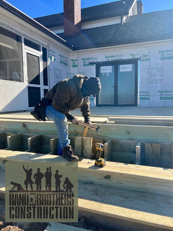 A man is working on a wooden deck in front of a house under construction.