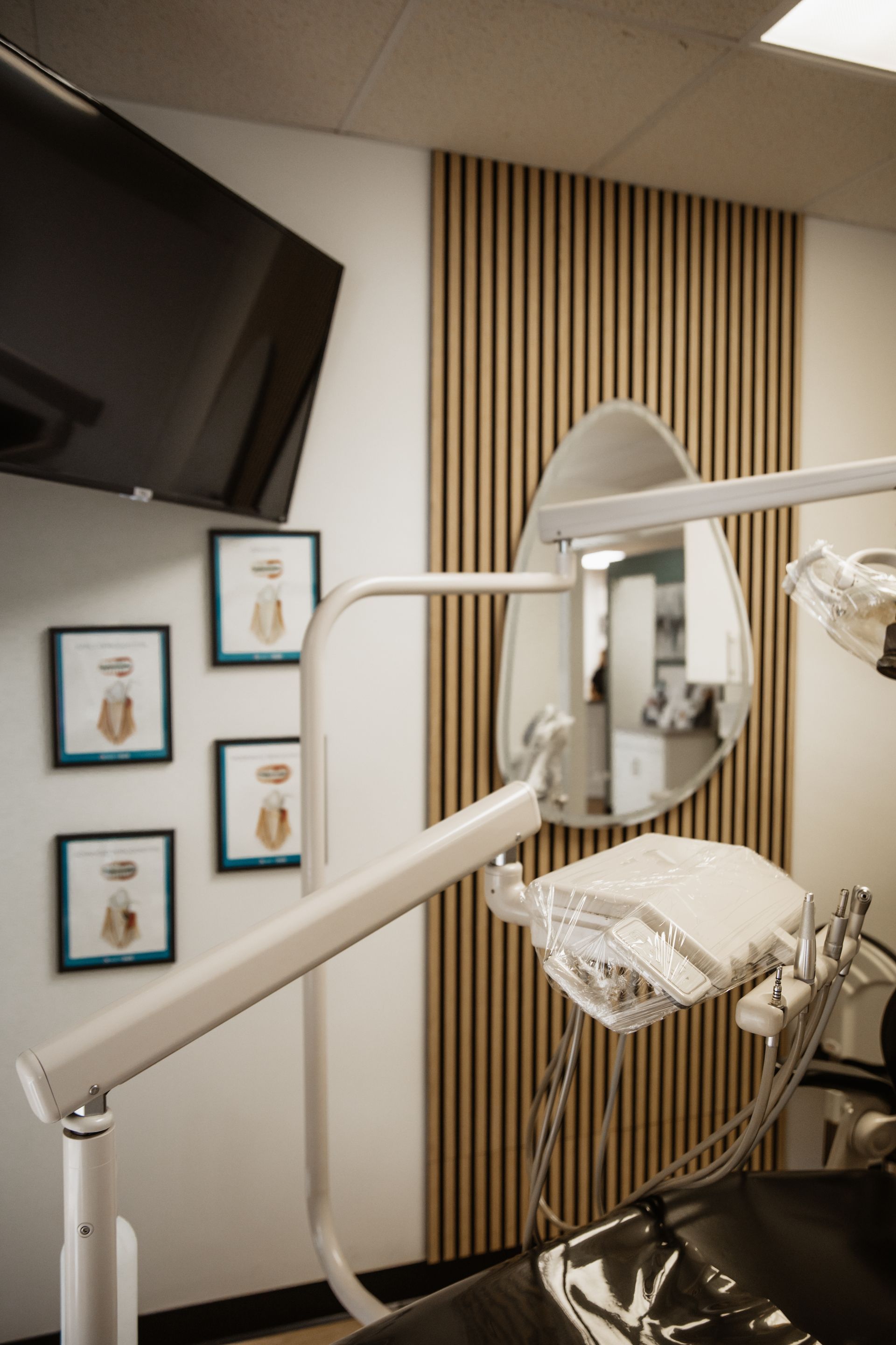 Dental office interior with a mounted TV, medical lamp, decorative wooden wall, and framed tooth diagrams.