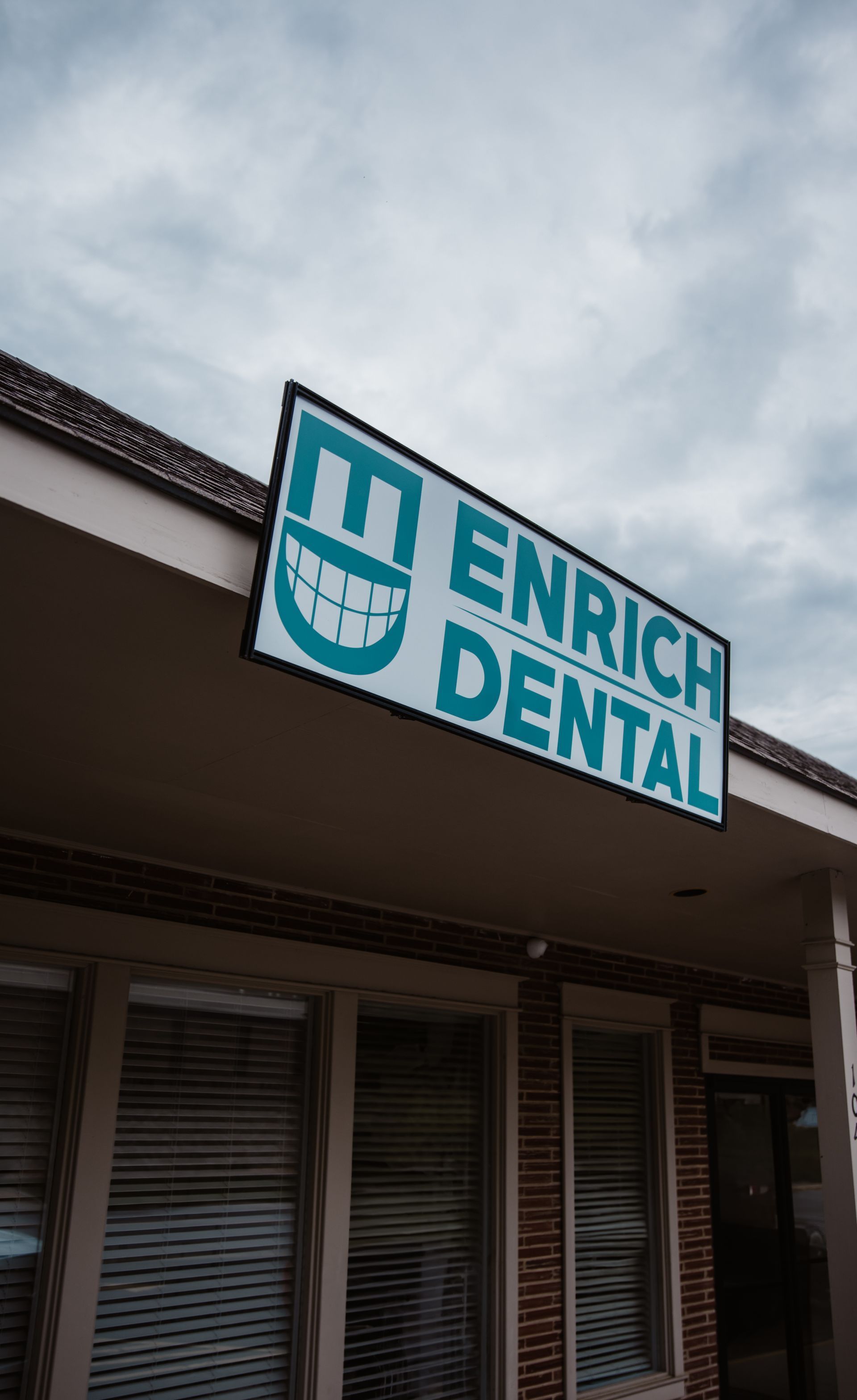 Sign for Enrich Dental, blue and white logo with smiling teeth, set against a cloudy sky.