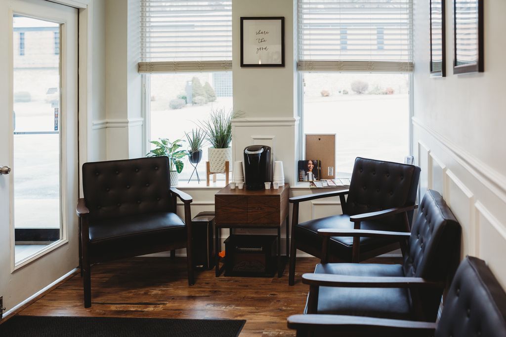 Waiting room with black chairs, wood floors, and two windows with blinds.